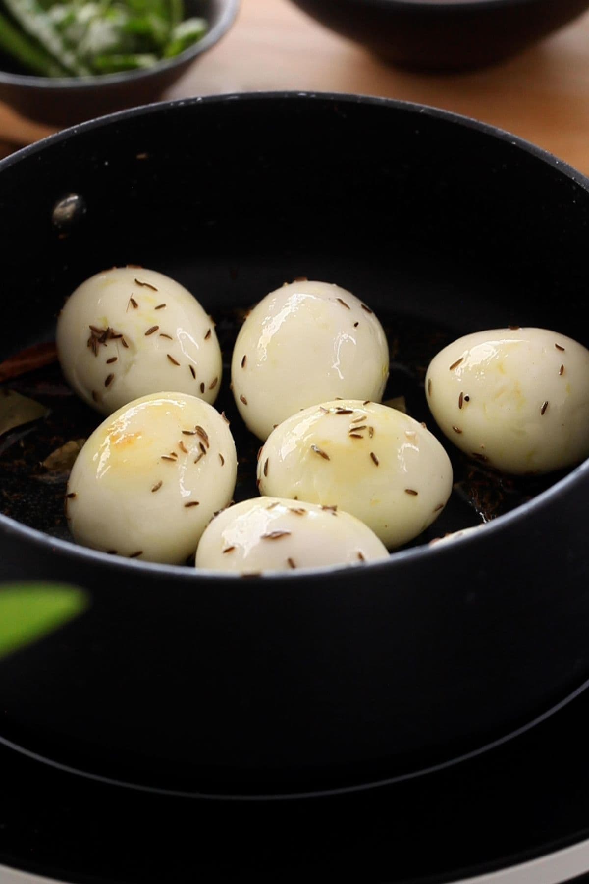 Hard boiled eggs are sauteed with whole spices in a black cooking pot.
