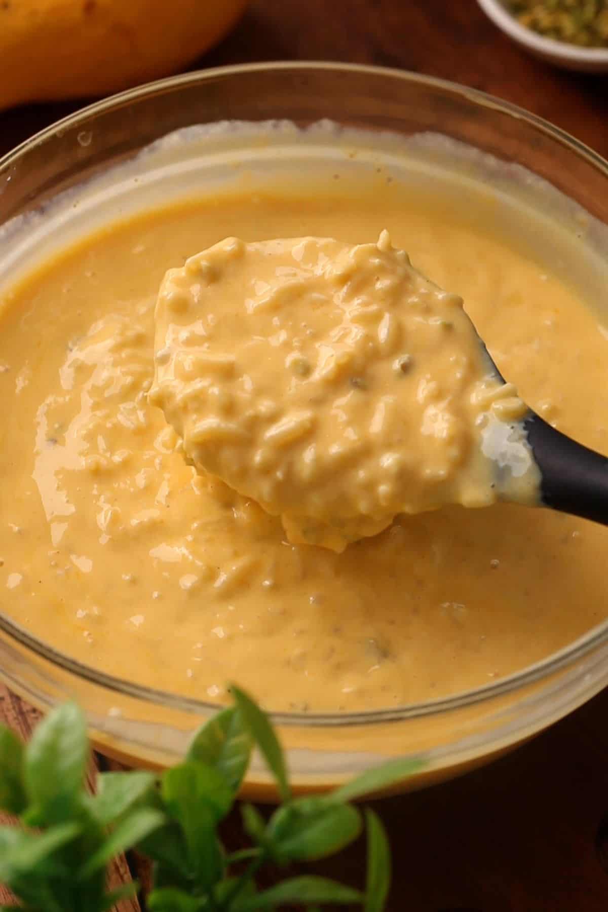 A close-up of a spoon scooping thick, creamy mango rice pudding.