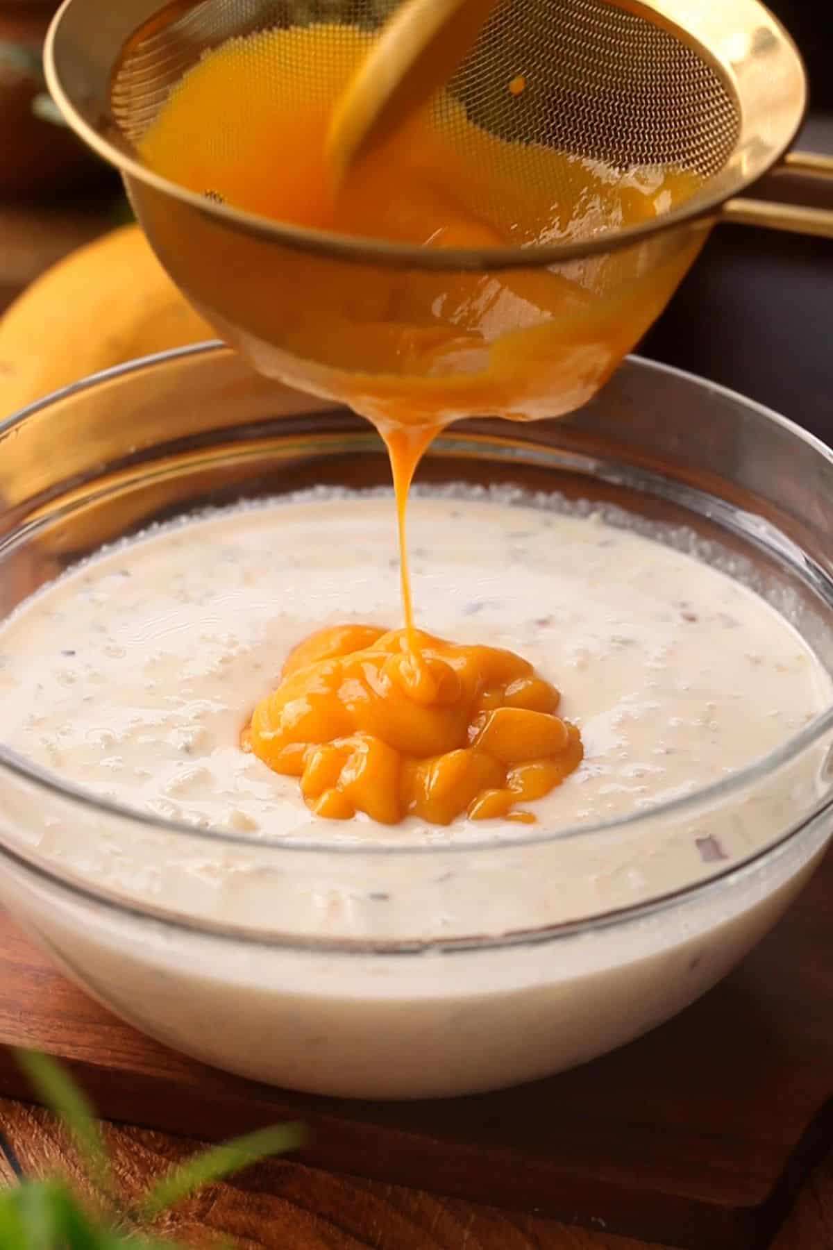 Straining mango puree using a gold colander over kheer.