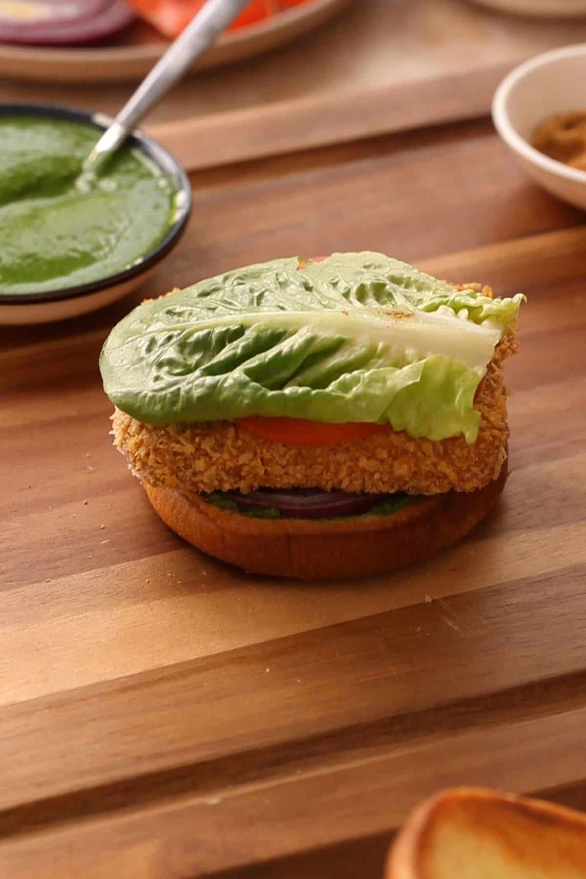 Close up of layering paneer burger on a wooden board.