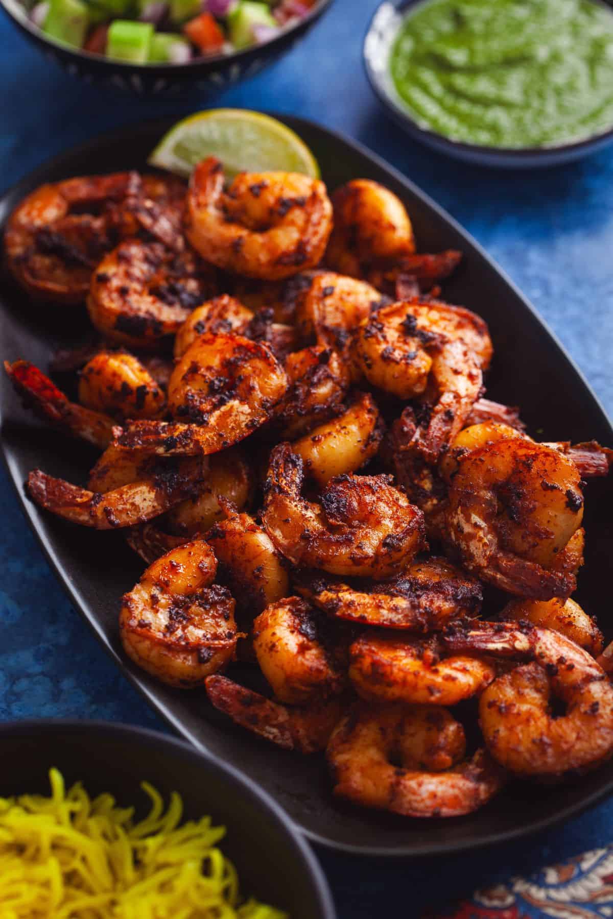 Side view of tandoori praws served on a black platter.