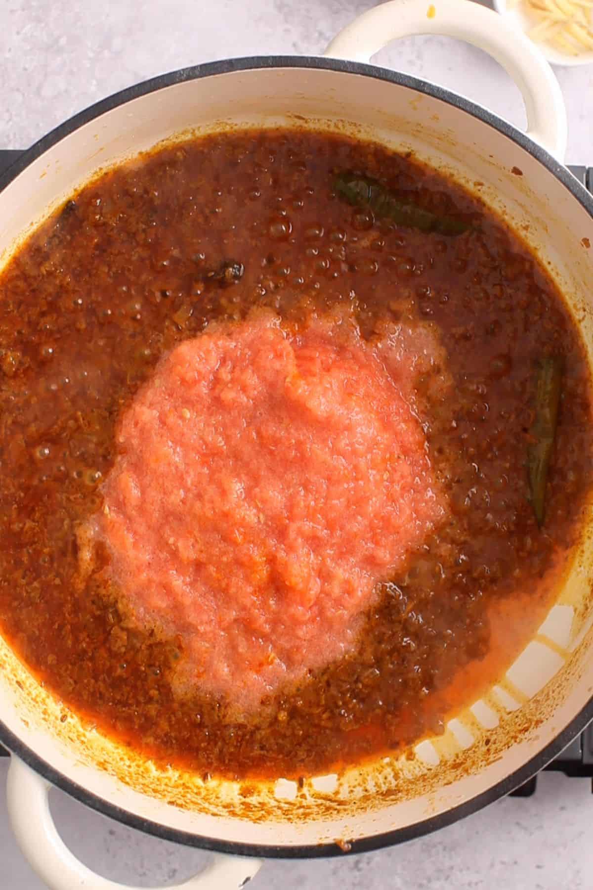 Pureed tomatoes are added to the sauteed spices and onions.