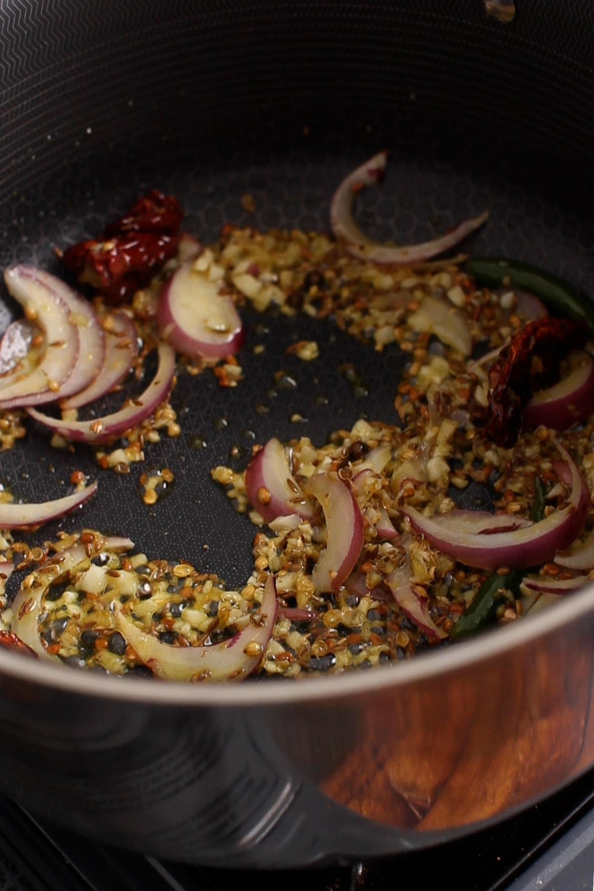 Aromatics and whole spices are cooked in oil in a deep, black cooking pot.