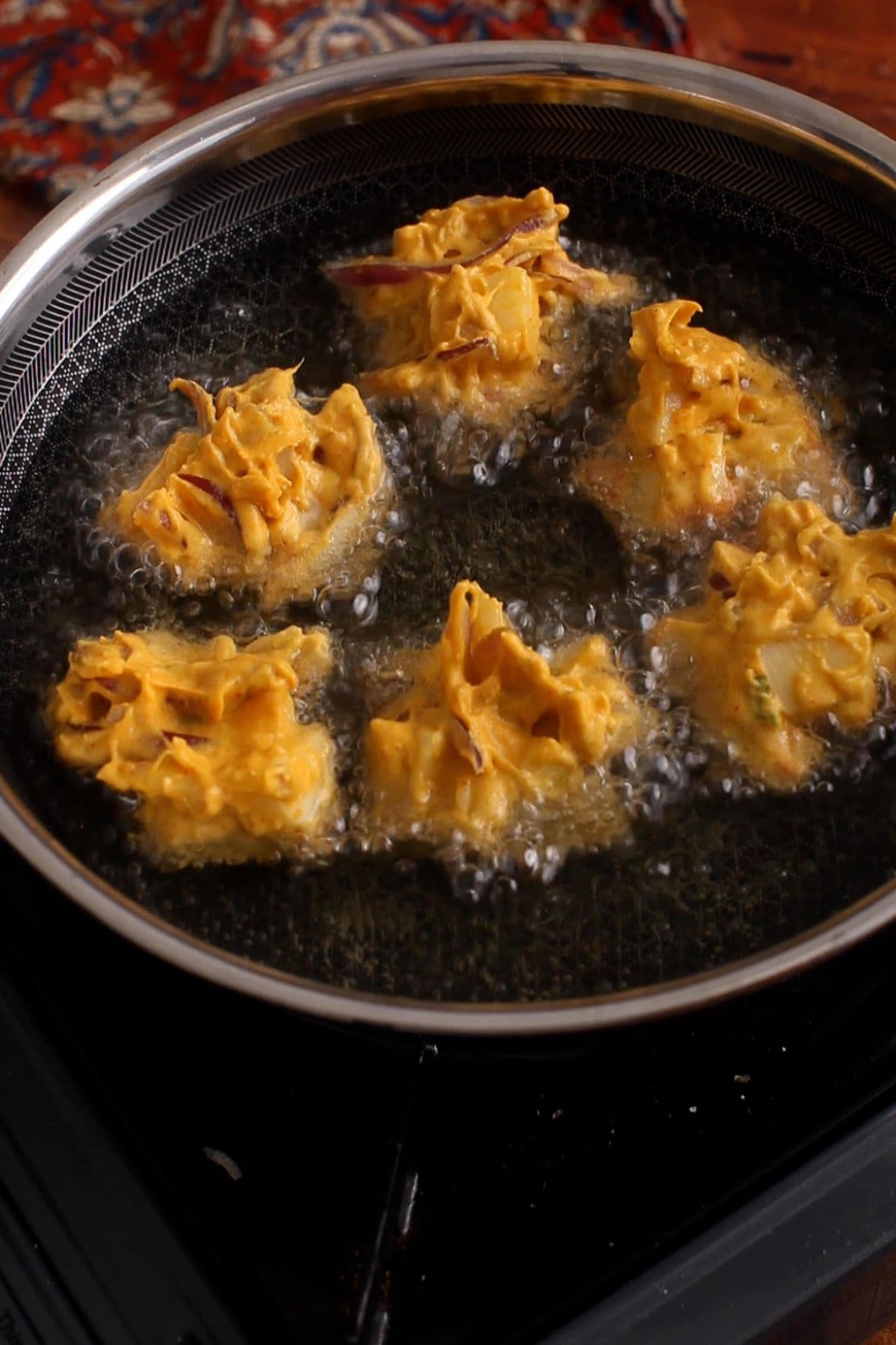 Pakora batter is added to hot oil in a black skillet.