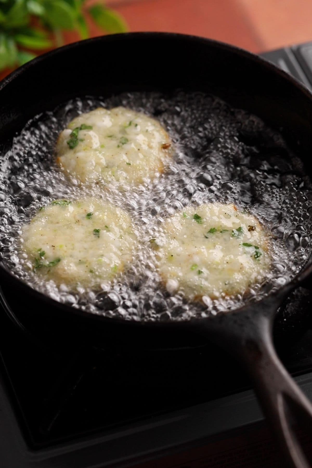 Sabudana vada are added for deep frying to hot oil in a cast iron skillet.