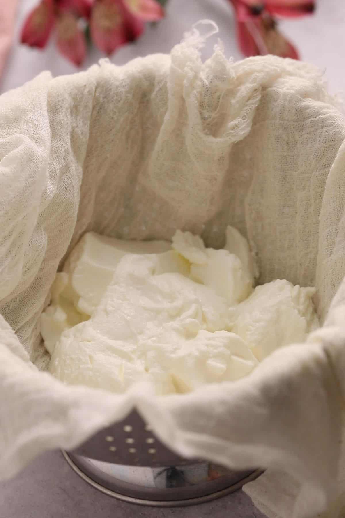 Strained plain yogurt placed in a cheesecloth over a stainless stell colander.