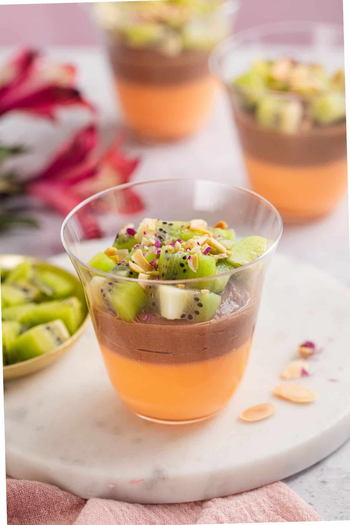 Chocolate Shrikhand layered with orange jelly and topped with kiwi in a glass dessert cup.