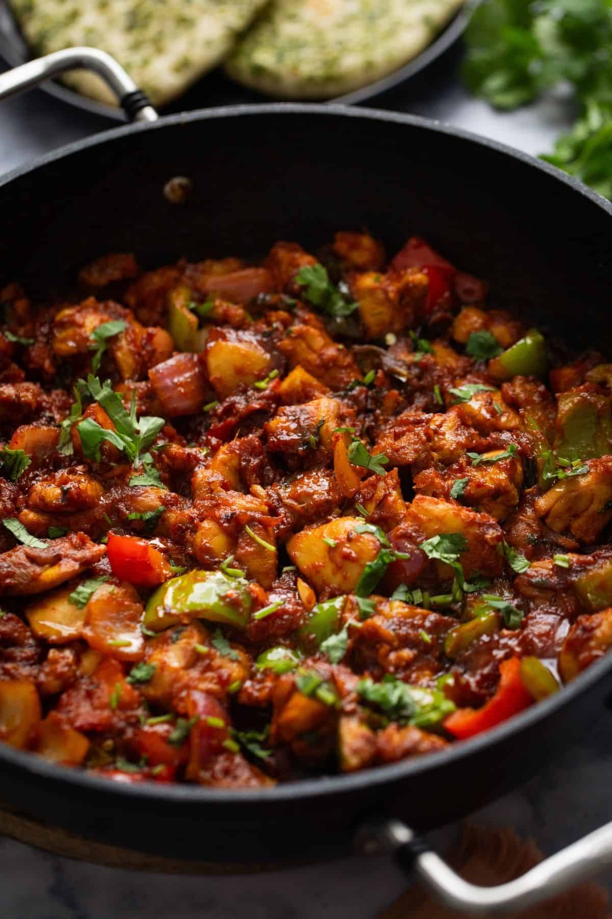 Side close up view of chicken jalfrezi in a black skillet.