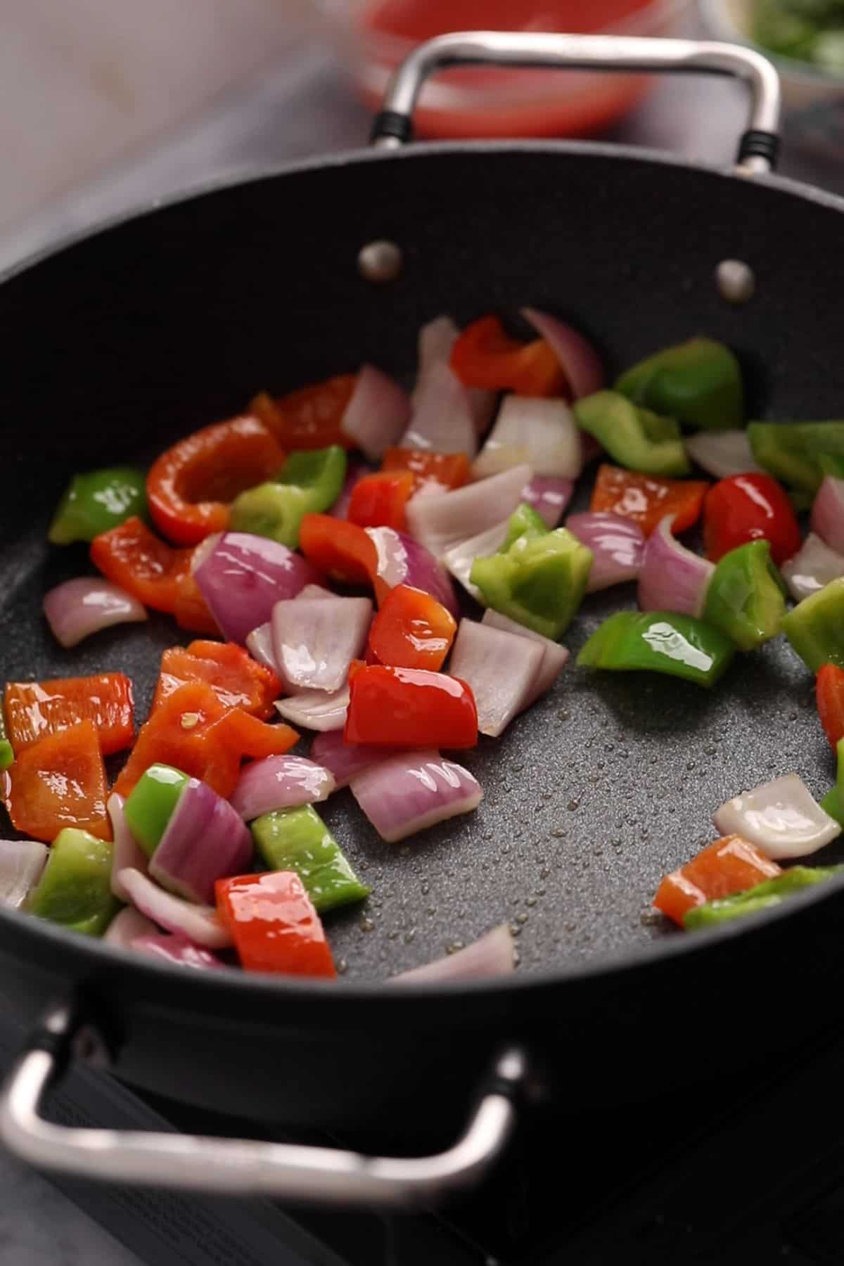 Bell peppers and onions stir frying in a large black skillet.