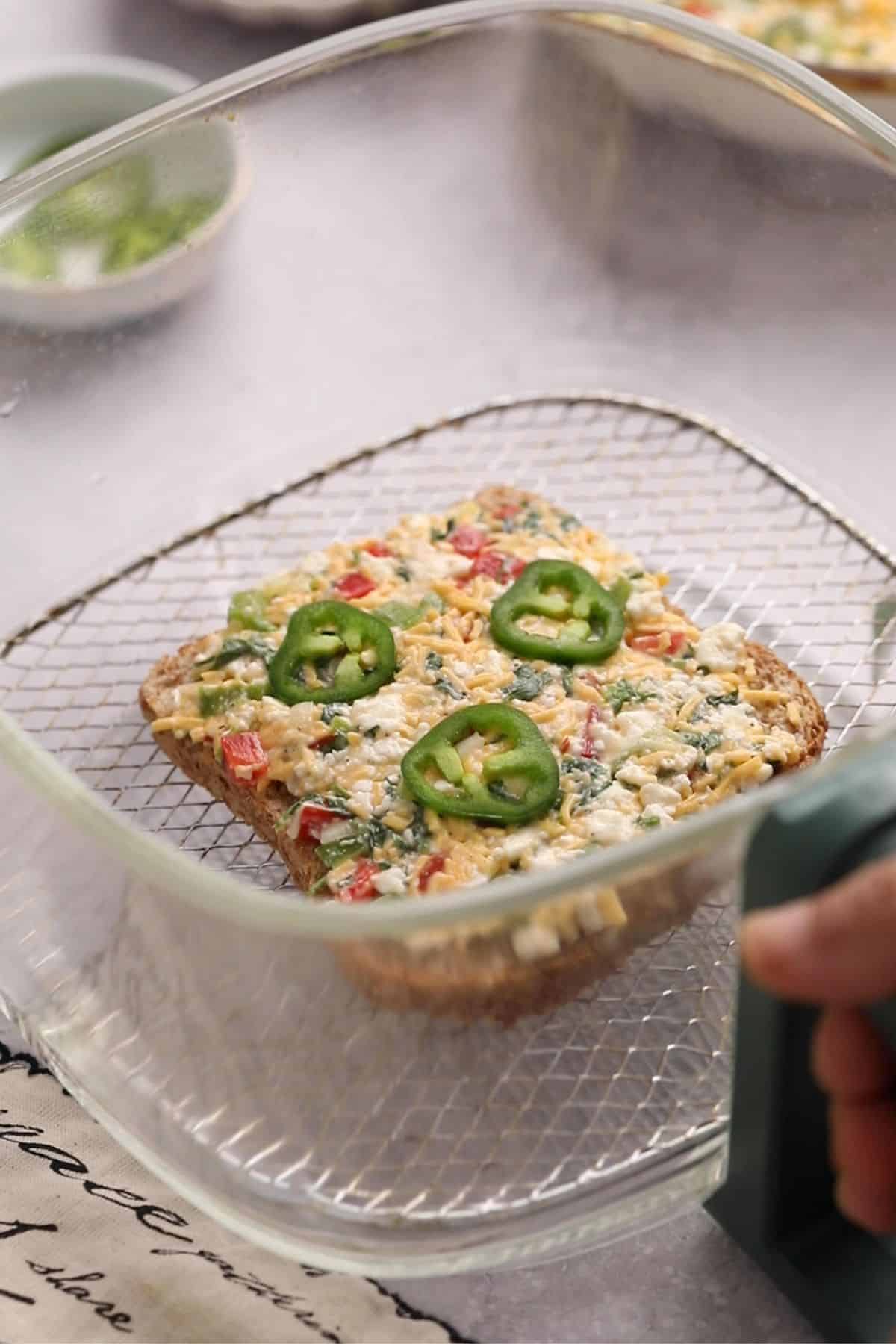 15-Minute Cottage Cheese Chilli Toast 13 Bread slice with cheese topping is placed on the rack of a glass airfryer basket.