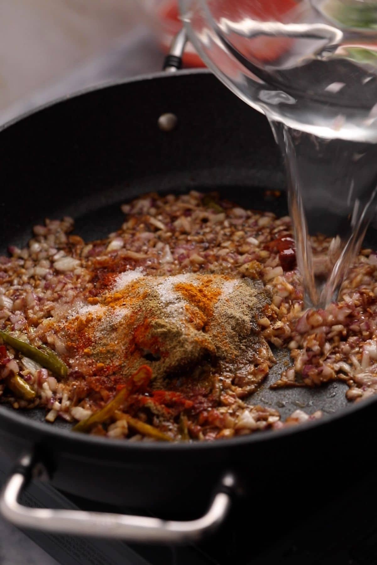 Ground spices are added to onions and water is poured.