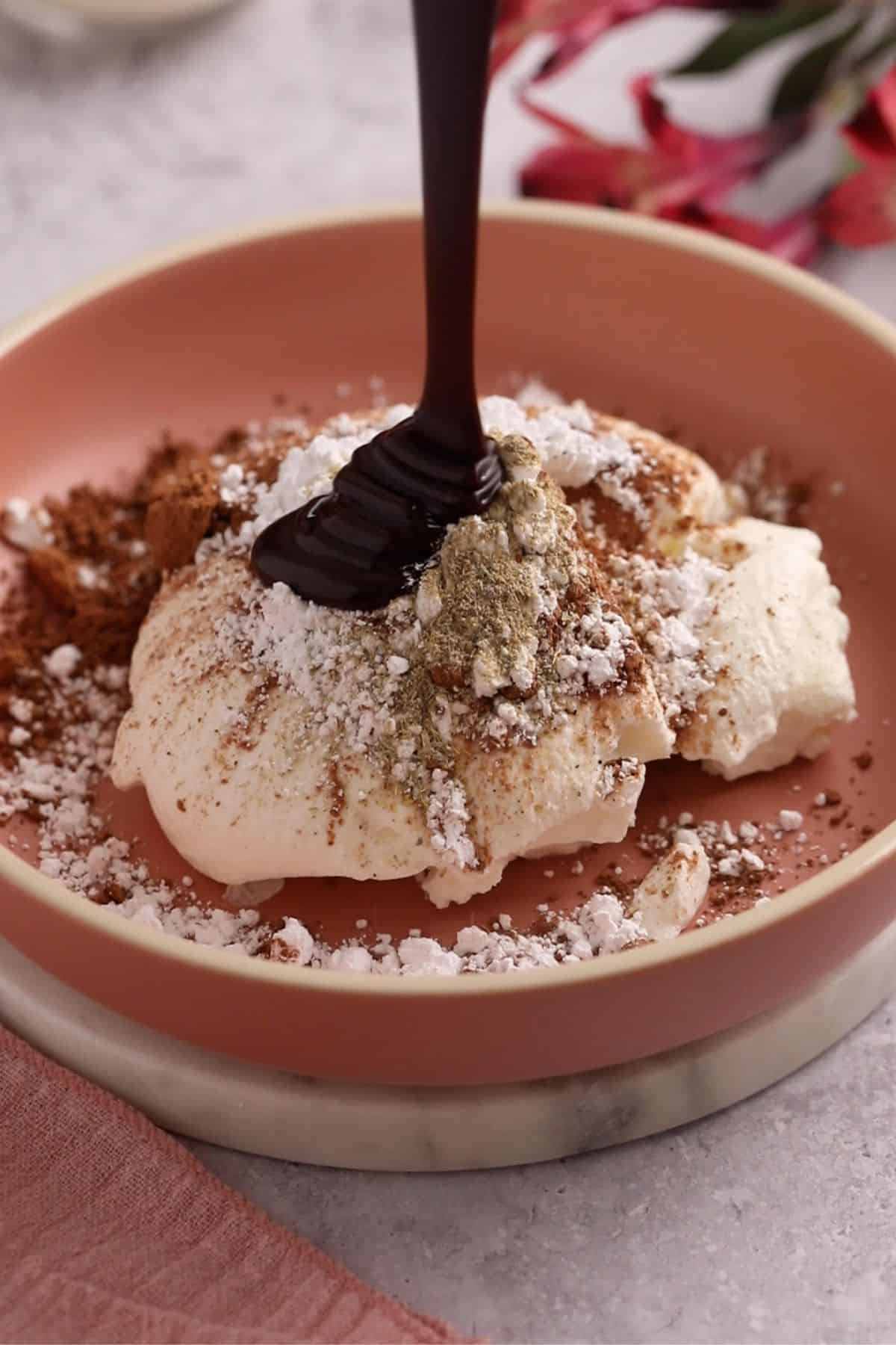 Chocolate, sugar, cardamom powder and cocoa are added to strained yogurt in a shallow pink bowl.