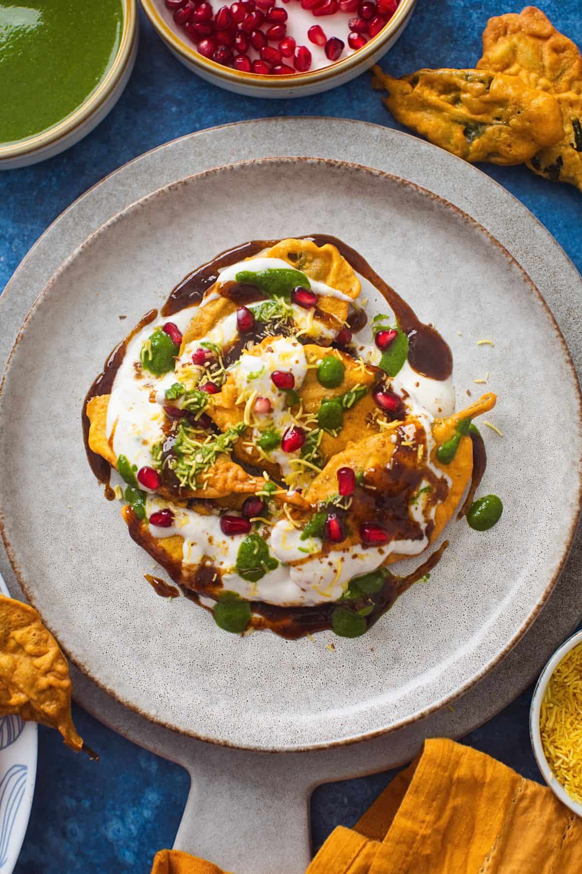 Delhi Style Palak Patta Chaat 5 Top down view of spinach leaf chaat with green chutney and pomegranate in small white dishes.