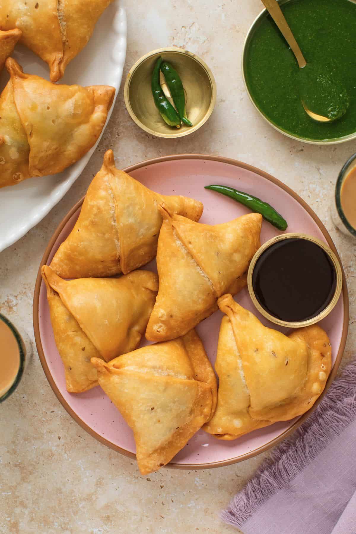 Classic Punjabi Samosa Recipe (Crispy & Flaky) 5 Top view of samosas on a pink plate with friend green chillies abd chutneys.