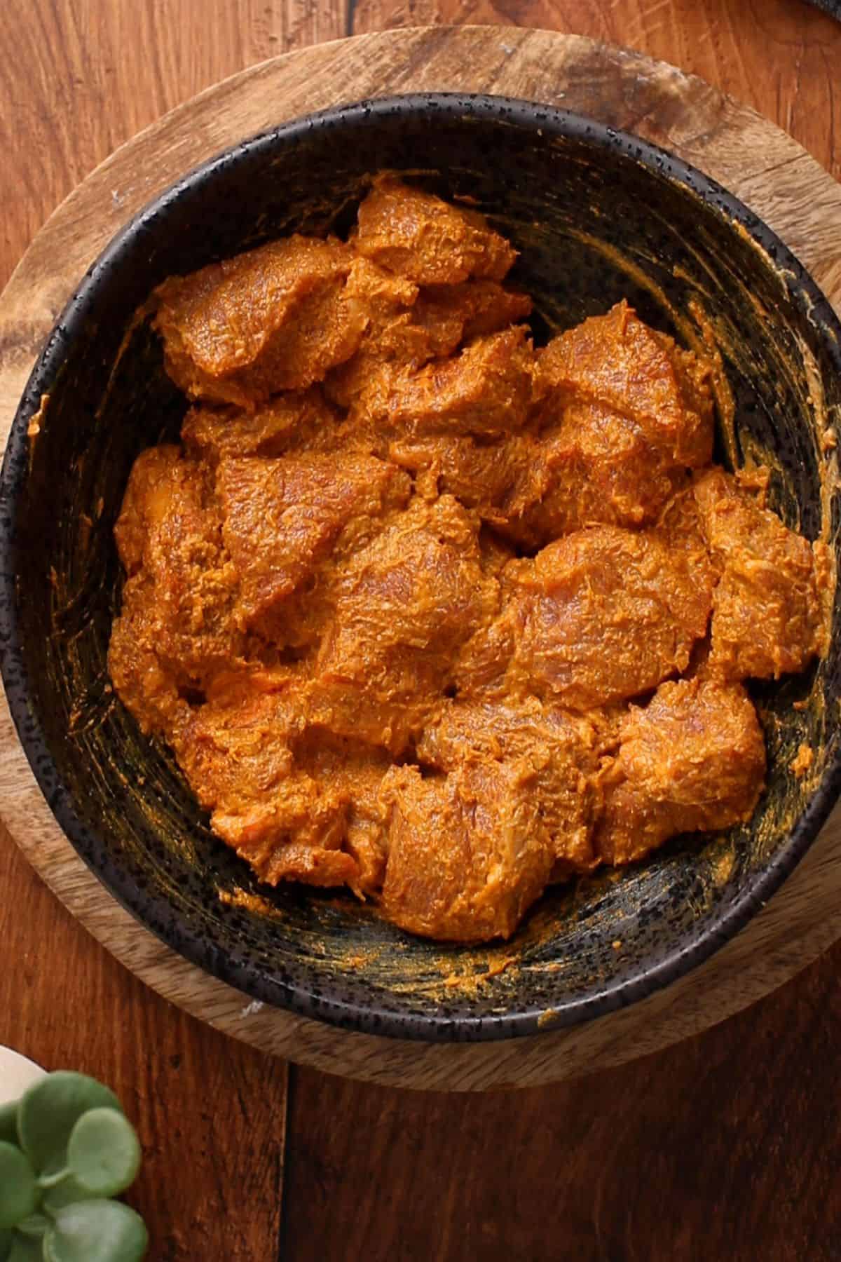 Restaurant-Style Lamb Korma (Rich & Creamy) 10 Lamb meat is coated in yogurt and spices in a black bowl placed on wooden surface.