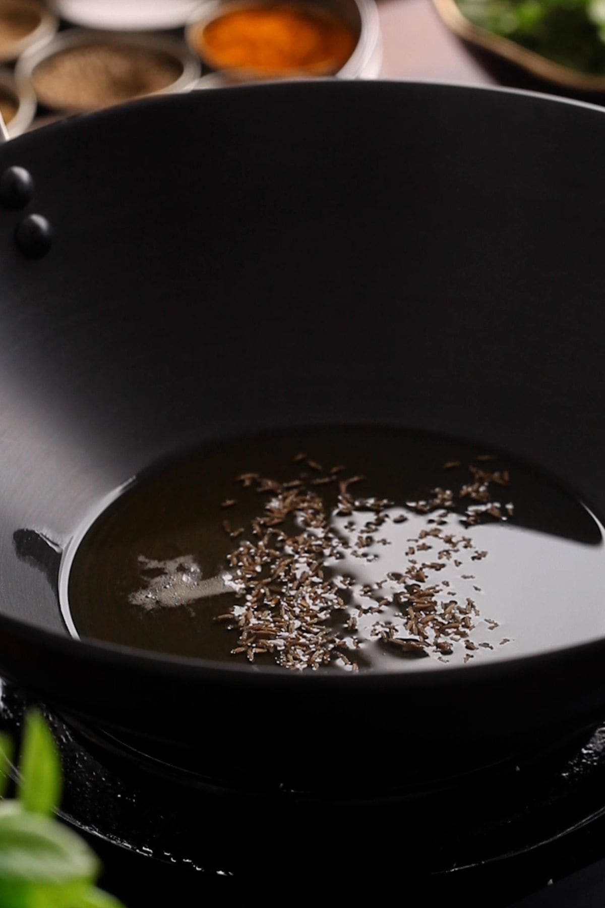 Cumin seeds are added to ghee in a black indian kadai. 