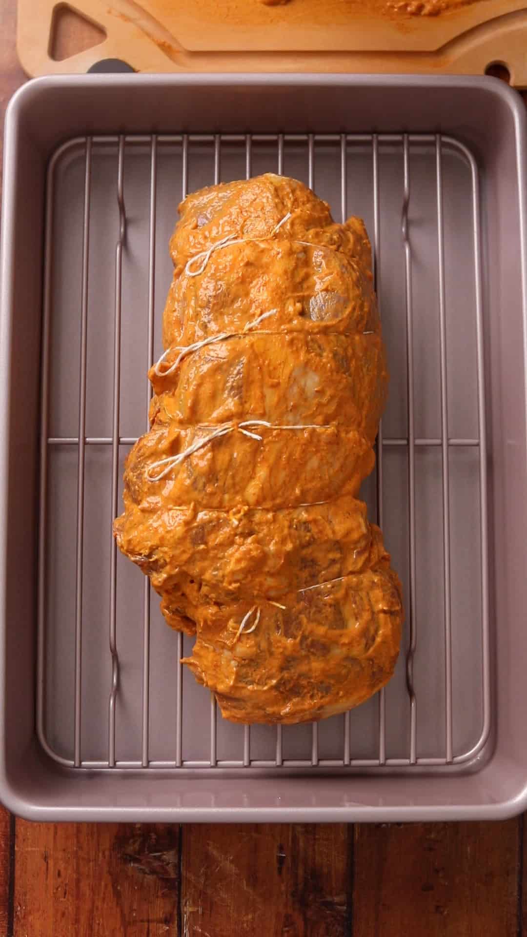 Marinated, tied lamb roast sits on a rack inside a roasting pan.