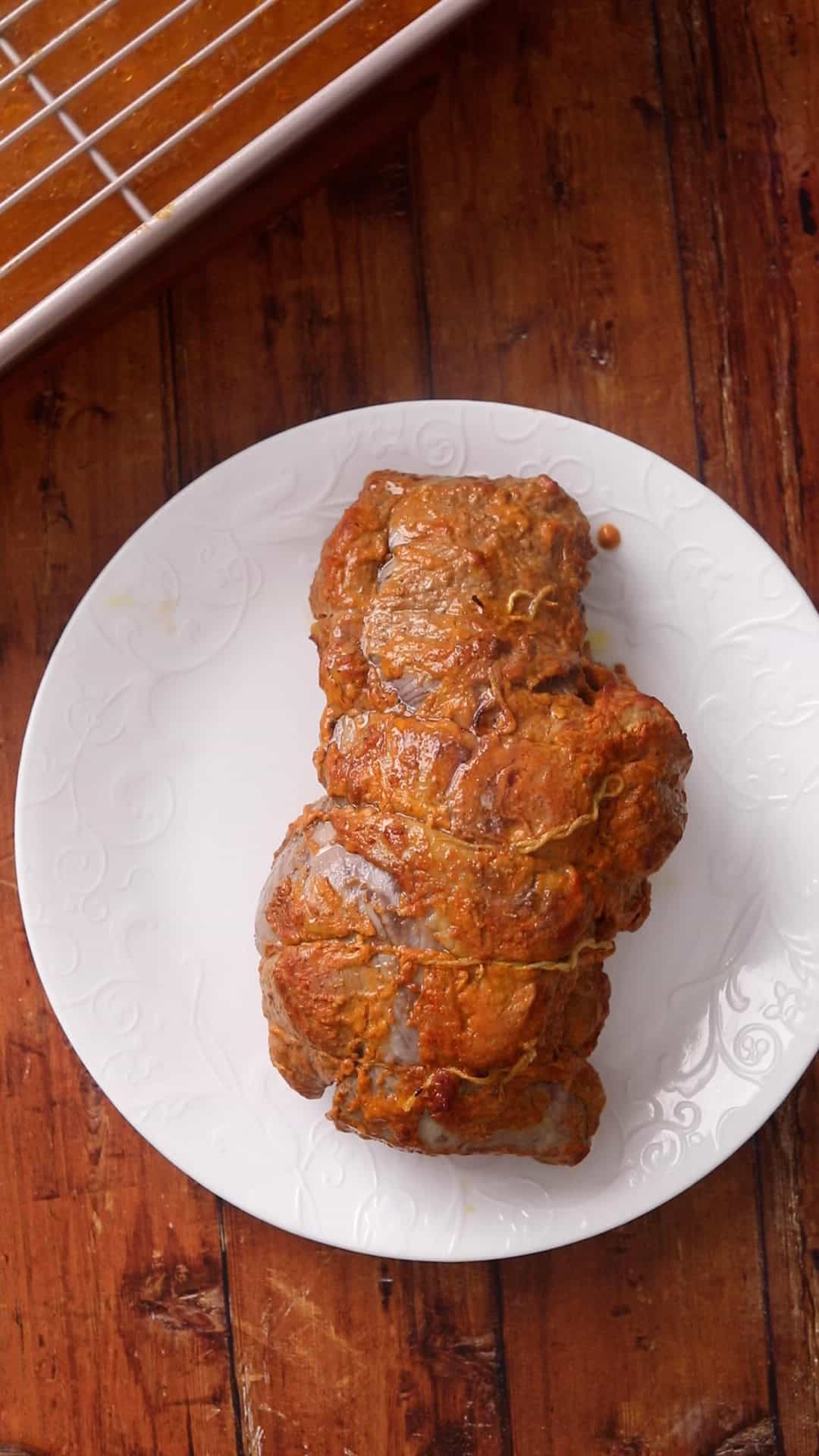 Lamb roast is placed on a white plate for resting.