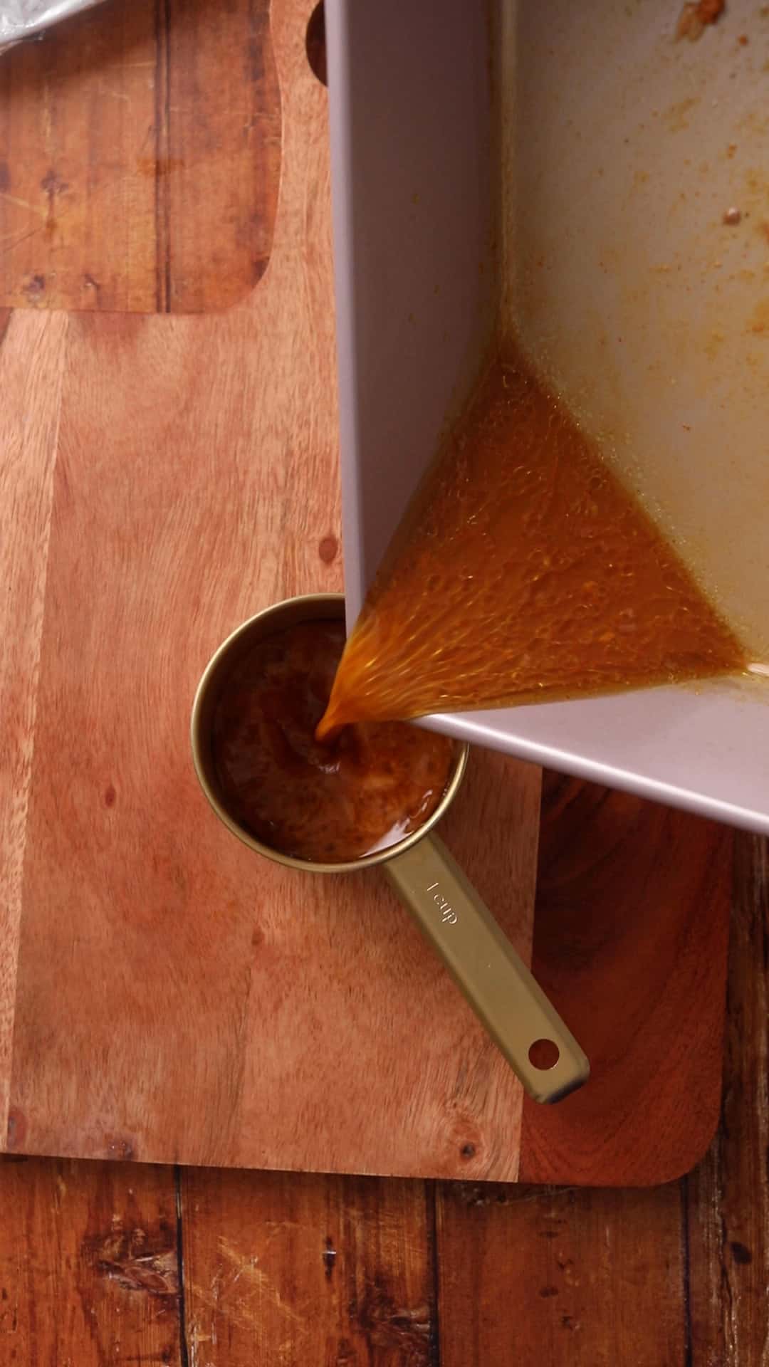 Pouring broth from cooking lamb roast to a gold measuring cup.