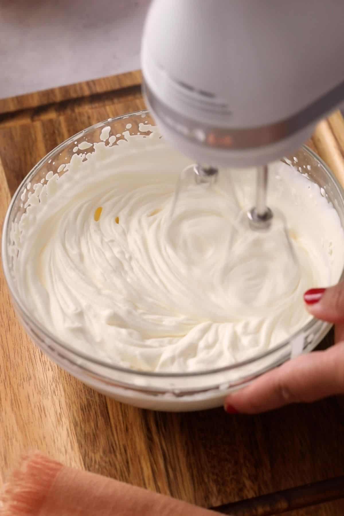 Beating heavy cream in a glass bowl to stiff peaks.