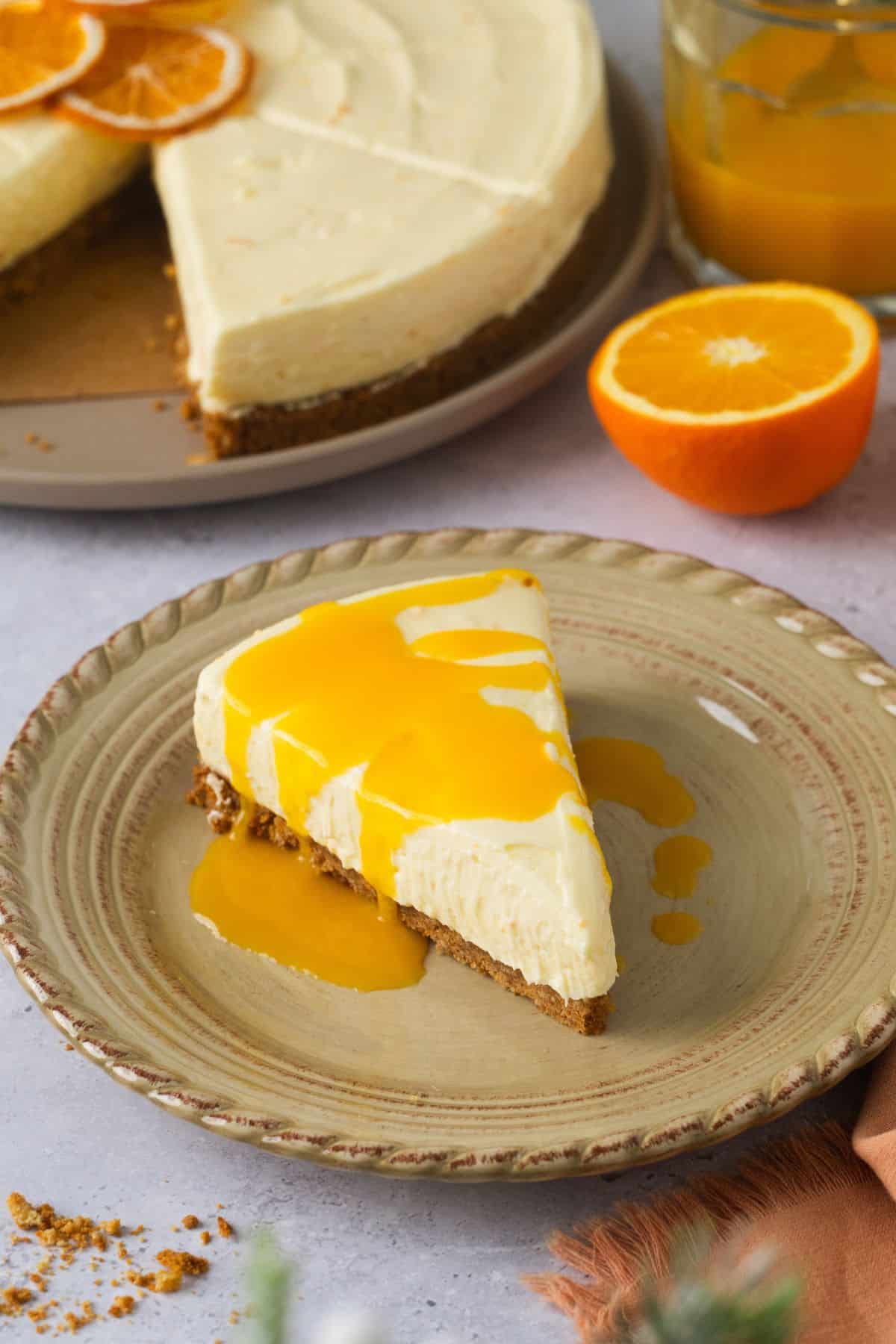 A slice of orange cheesecake placed on a beige plate with cut up fresh orange in background.