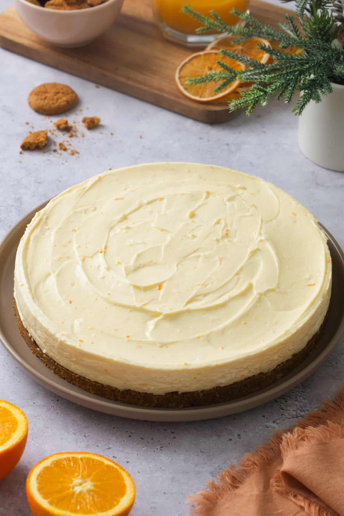 Whole nobake orange cheesecake placed on a grey backgroud with ginger snaps in background.