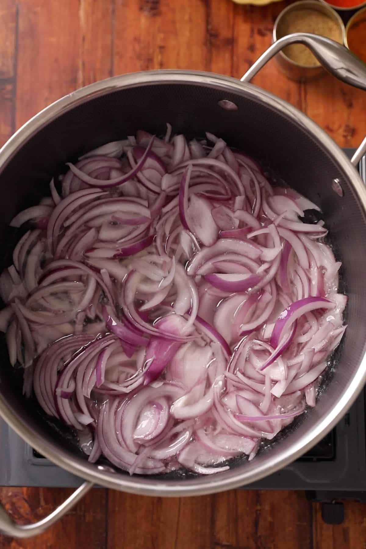 Sliced red onions are added to hot oil for frying.