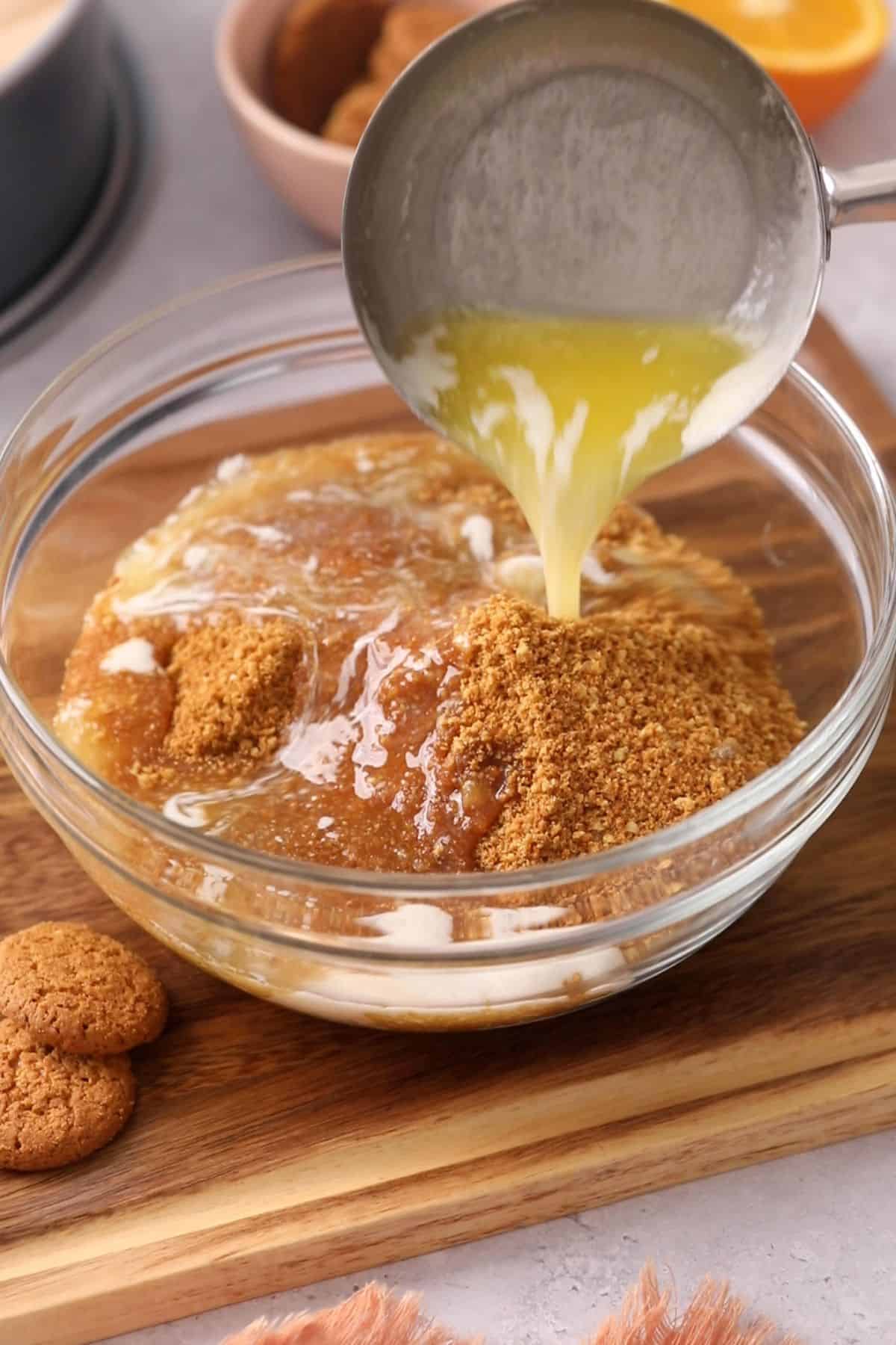 Adding melted butter to ginger snap crumbs placed in a glass bowl.