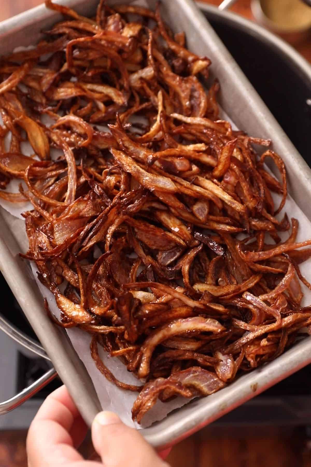 Golden fried onions are taken out in a small aluminumbaking tray. 