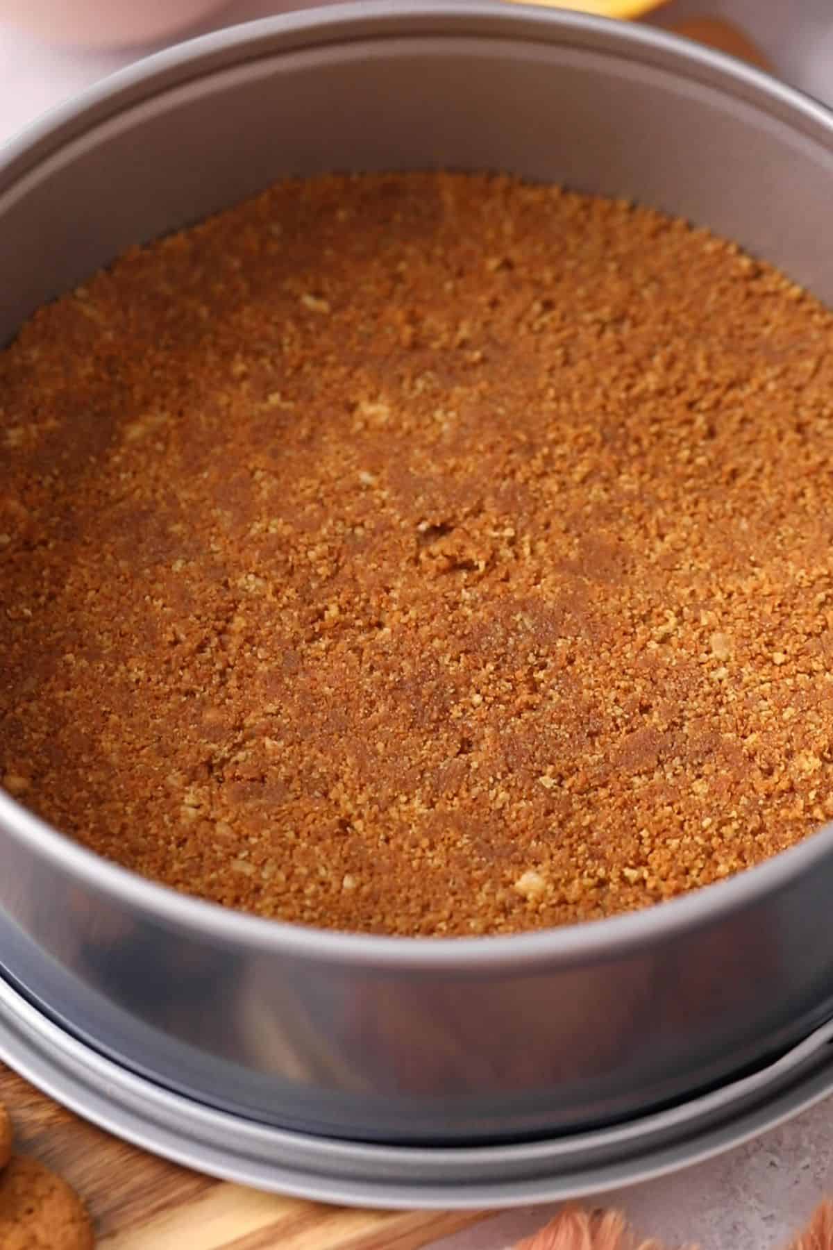 Ginger crumb mixture is pressed down to form the cheesecake crust in a sprinform pan.