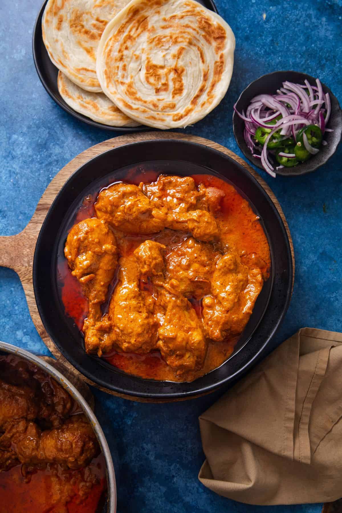 Overhead image of delhi chicken korma served with indian flatbreads on a blue background.
