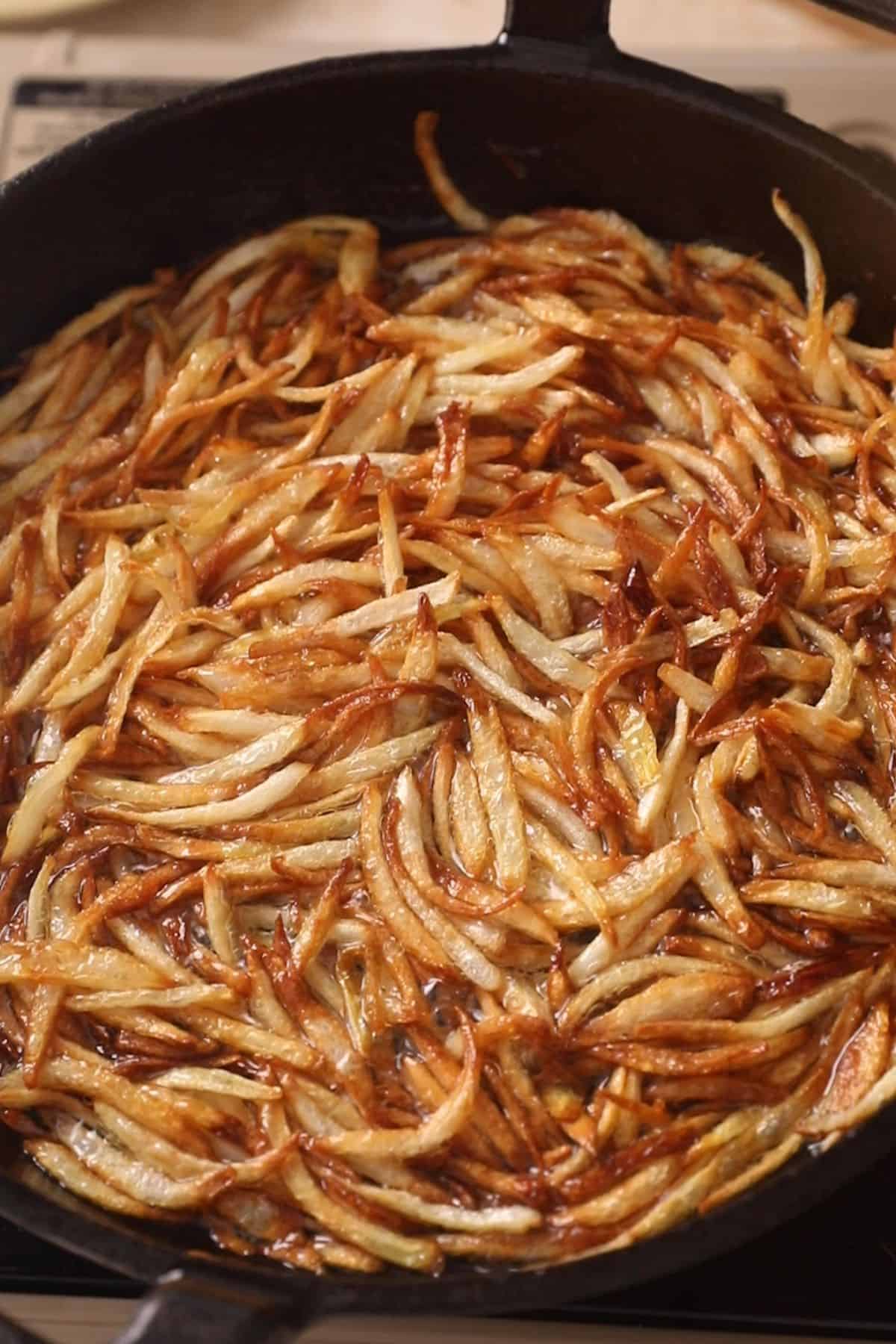 Golden brown, crispy onions in hot oil in a black cast iron skillet.