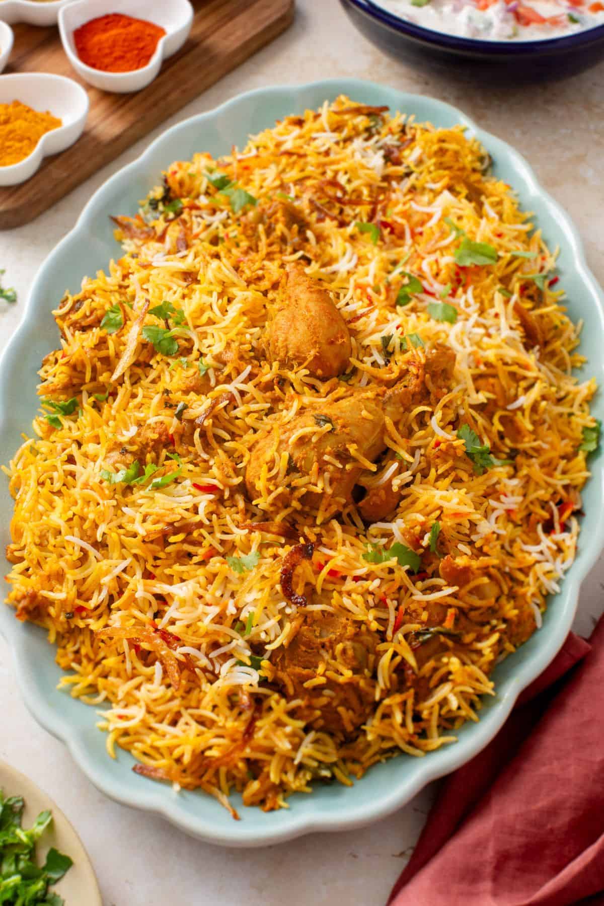 A platter of chicken biryani with fluffy basmati rice with pieces of chicken, garnished with fresh herbs and deep fried onions.