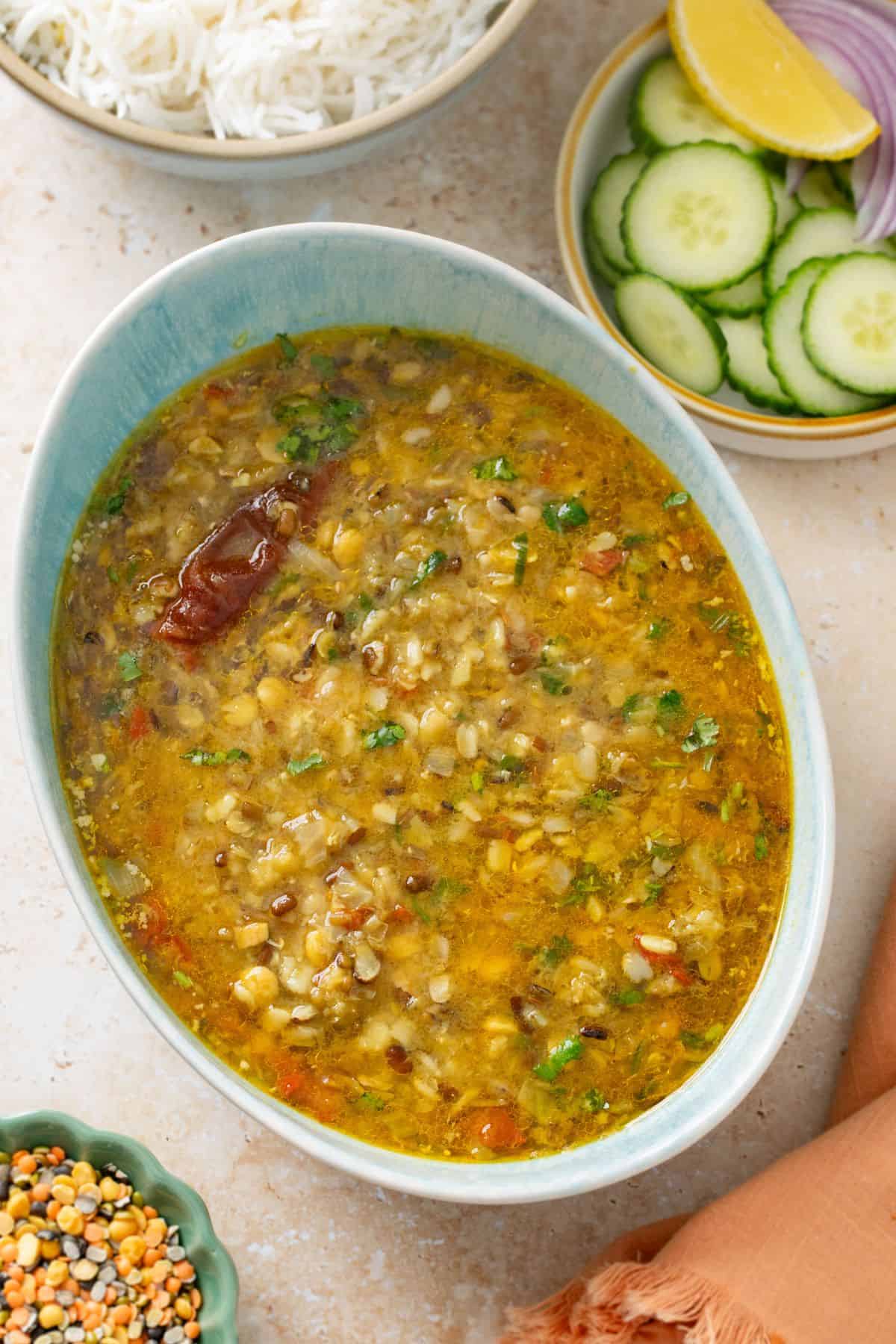 Mixed dal is served in an oval turquoise bowl with rice and salad. 