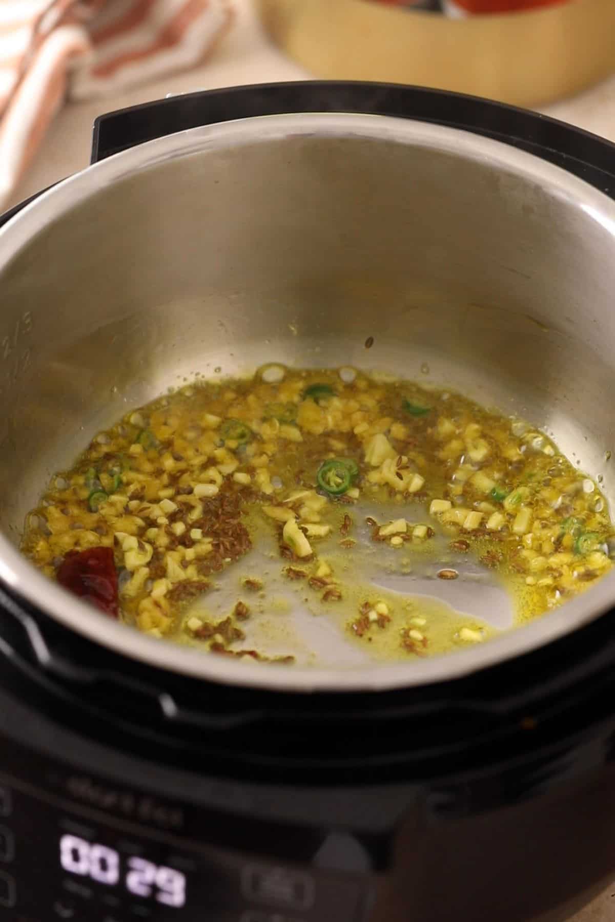 Whole spices and aromatics are frying in oil in steel insert of instant pot.