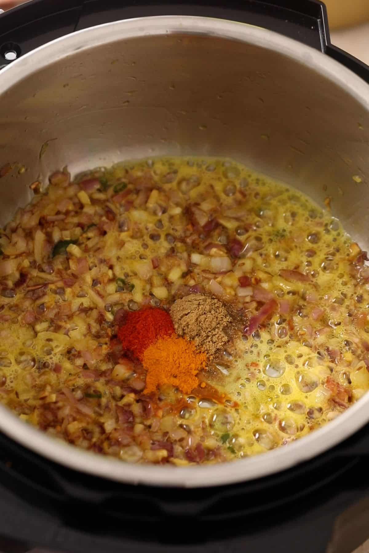 Ground spices are added to browned onions with a splash of water.