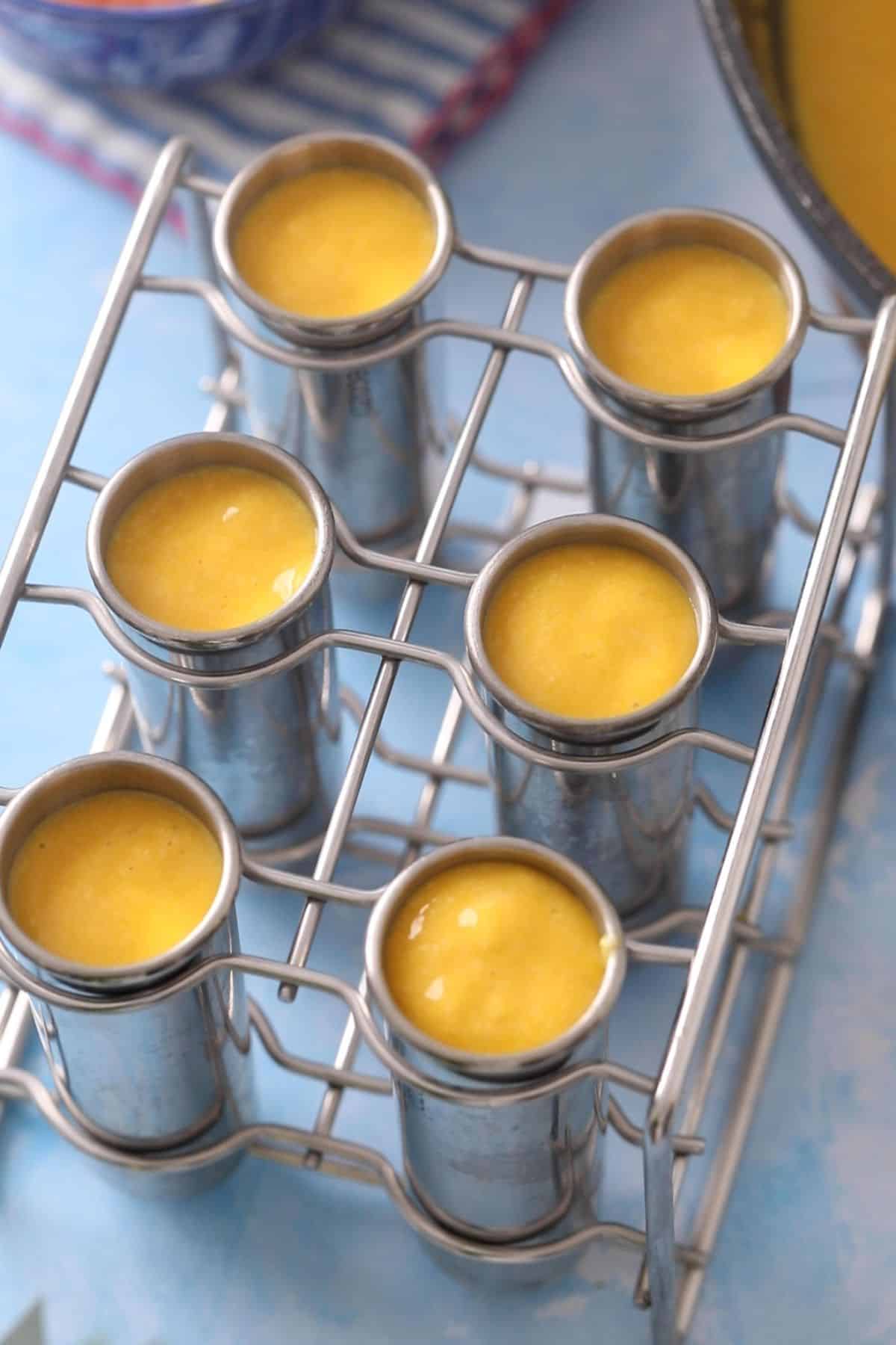 Mango kulfi milk mixture is poured into stainless steel moulds.