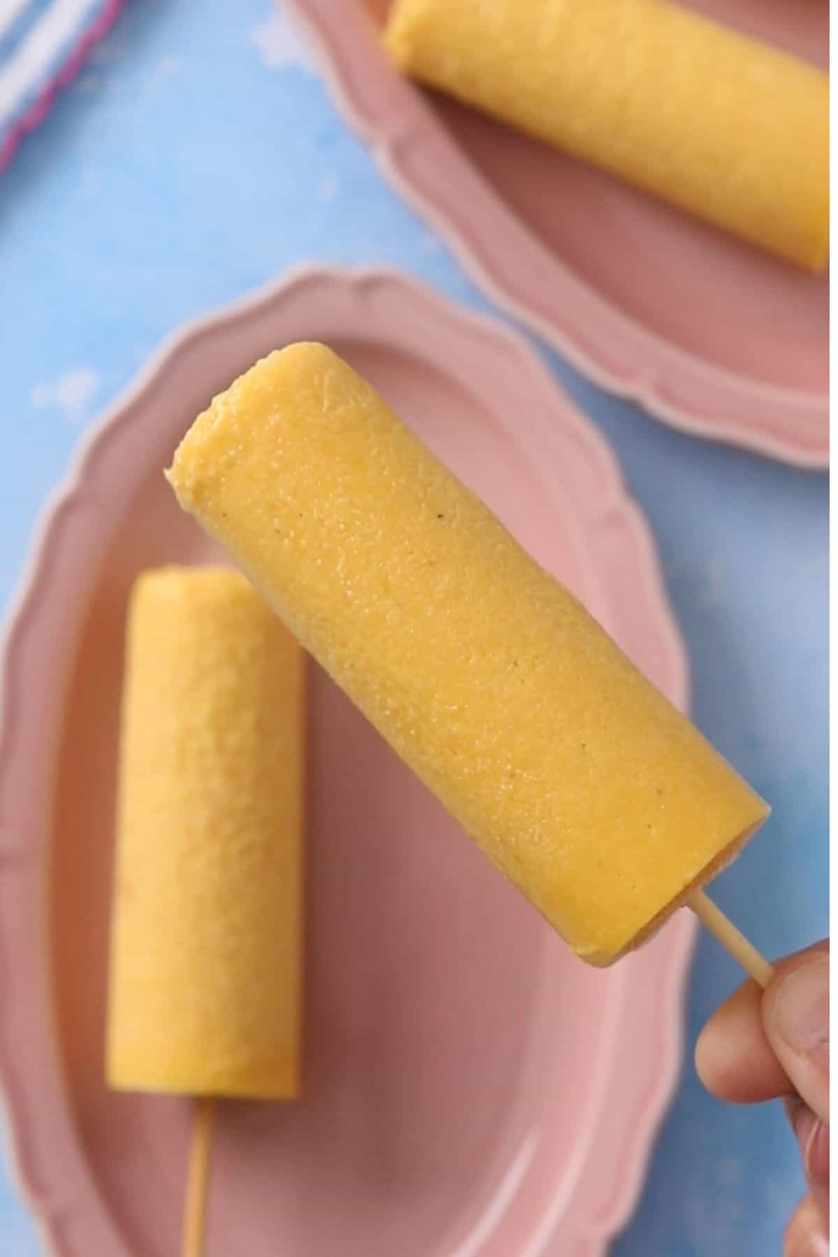 Mango kulfi is unmoulded and held by hand.
