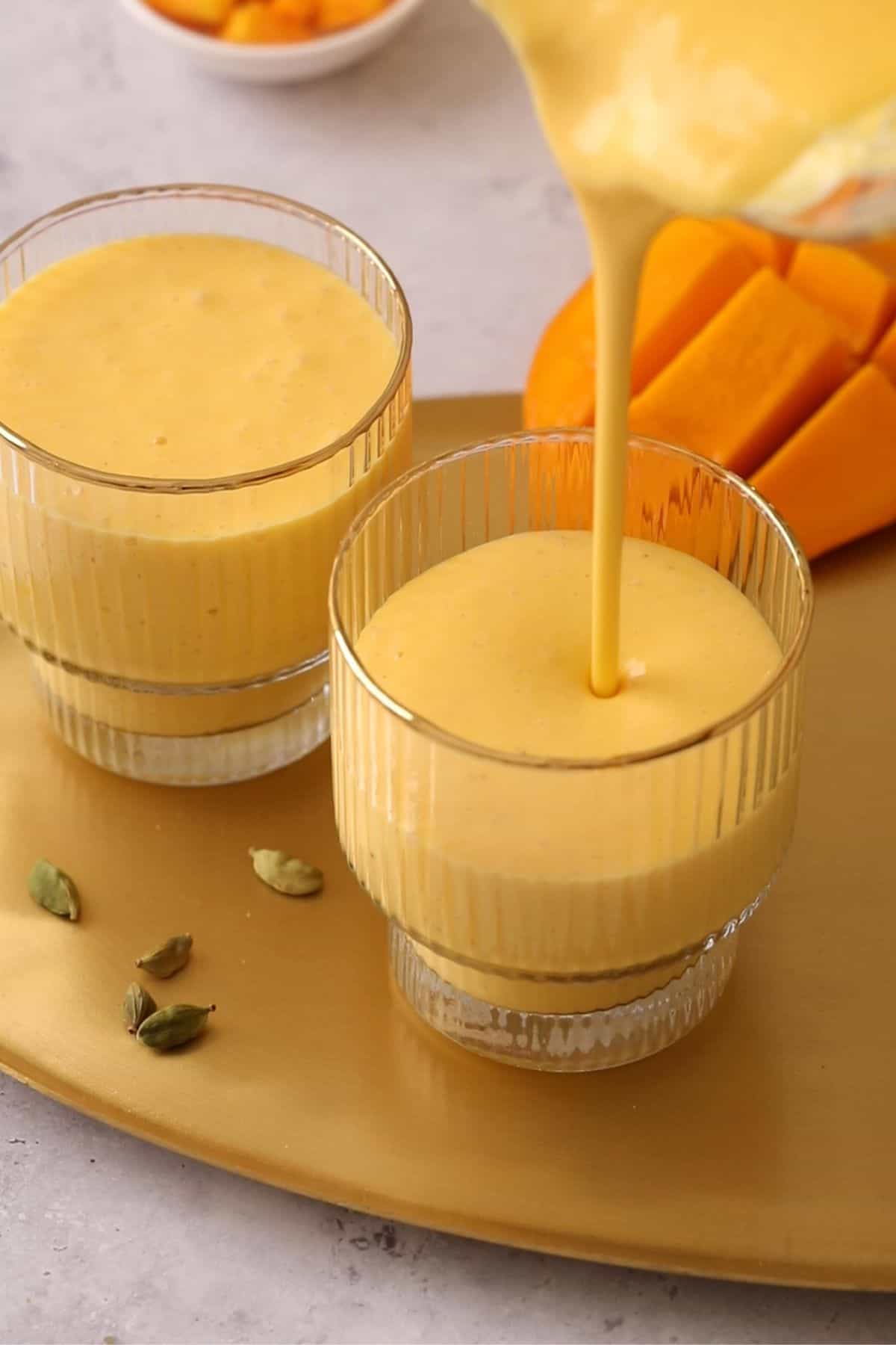 Pouring lassi into gold rimmed fluted glasses.