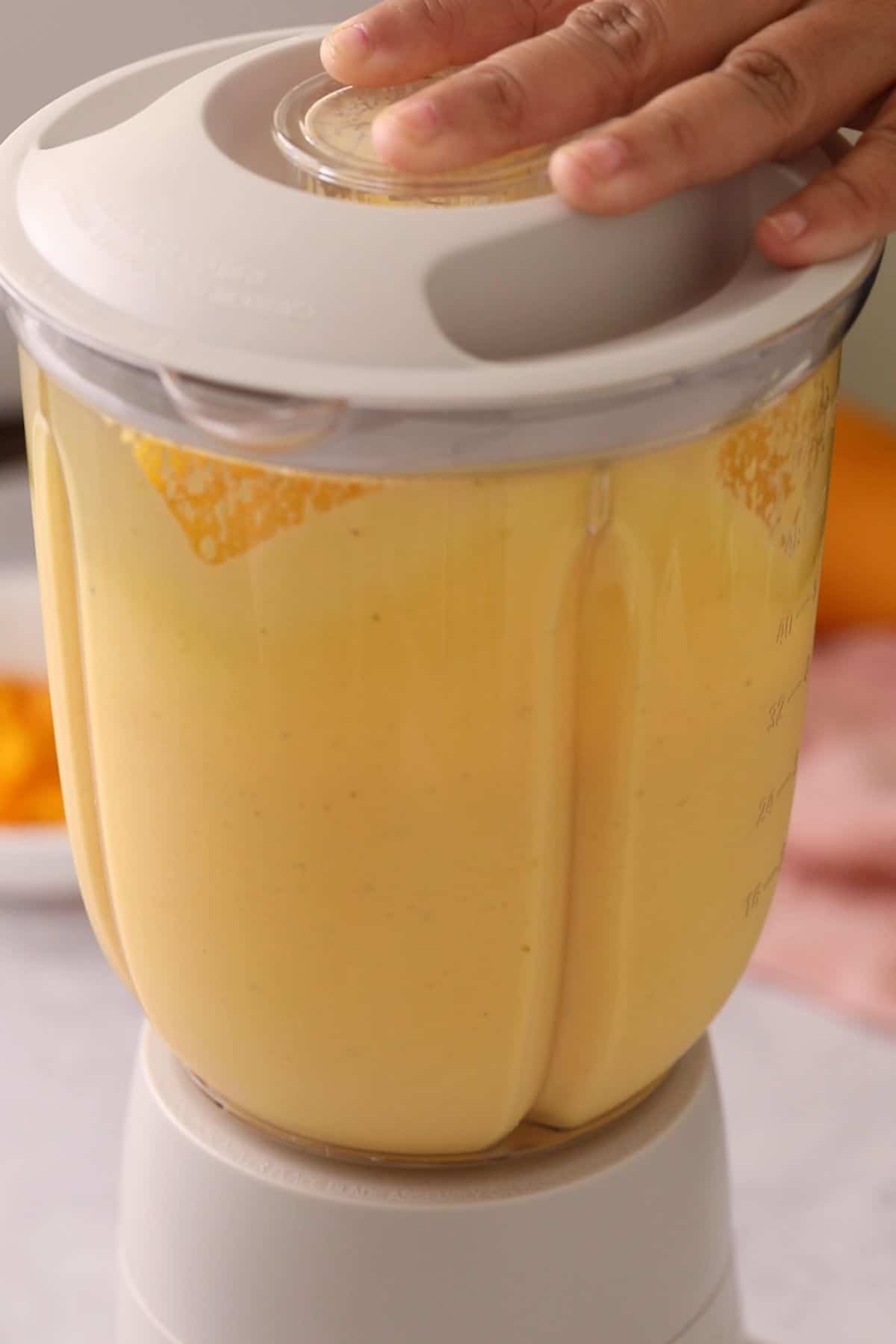 Mango lassi is being blended in a beige blender jar.