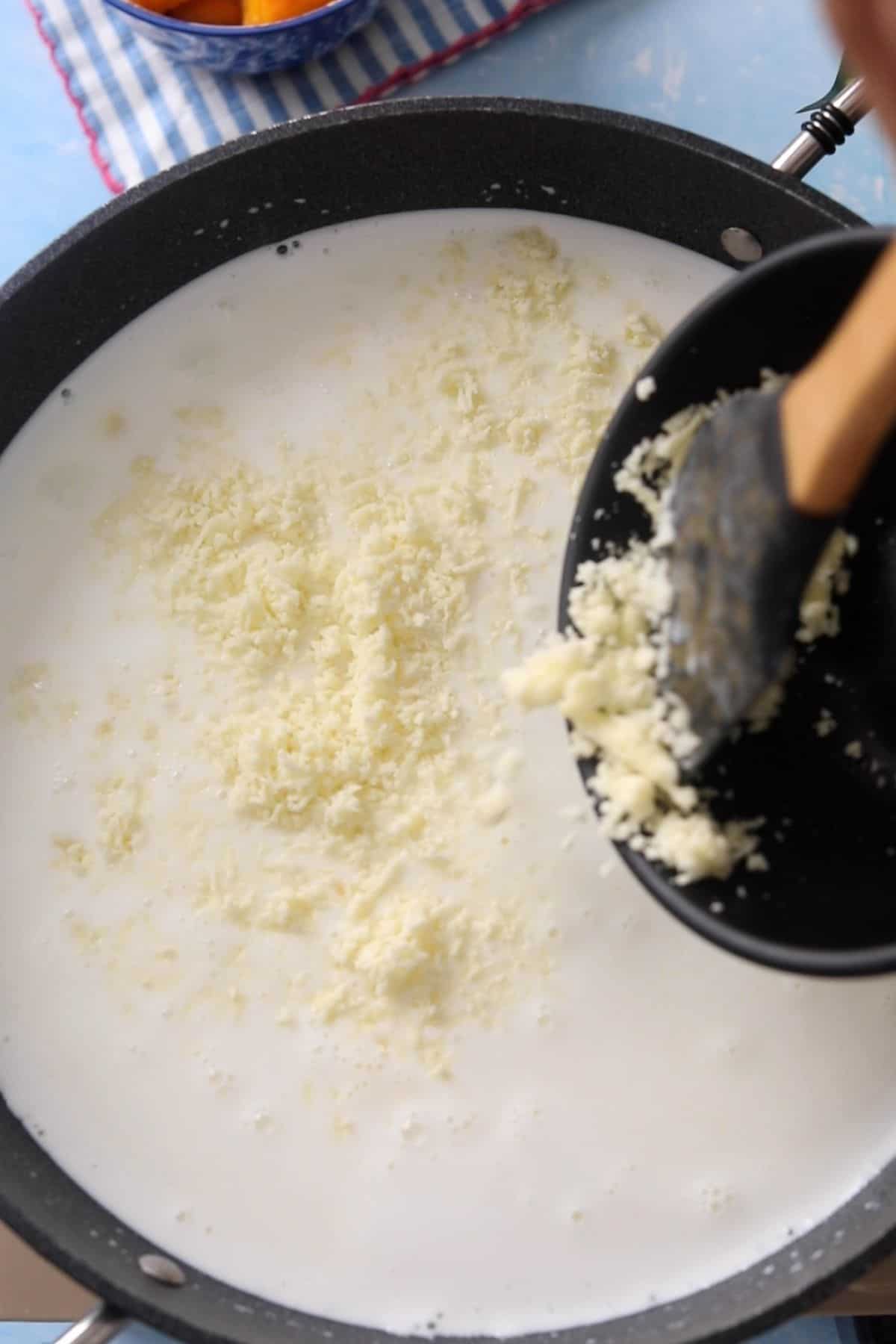 Grated khoya is added to a large pot of milk.