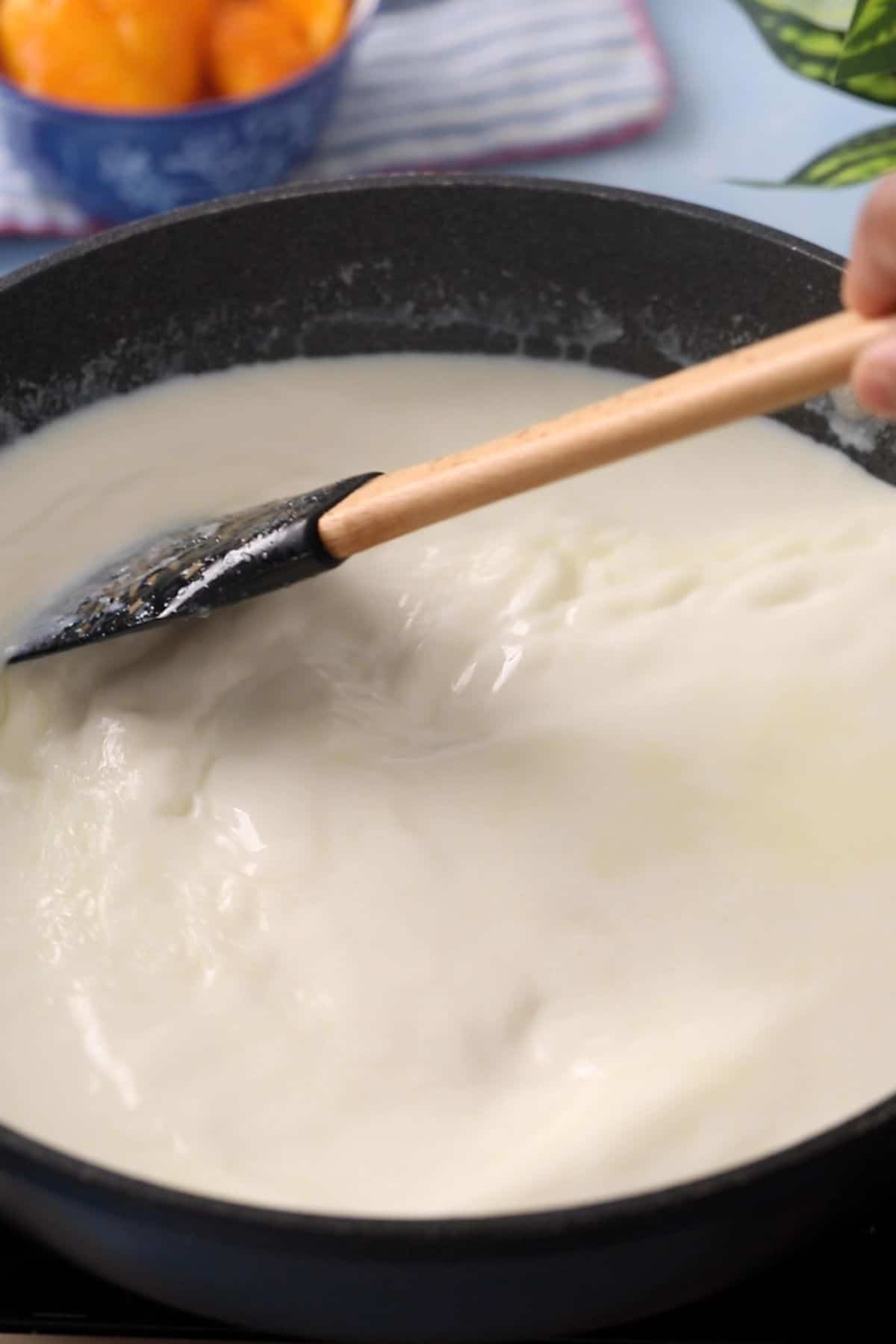 Milk mixture is stirred using a black spatula.
