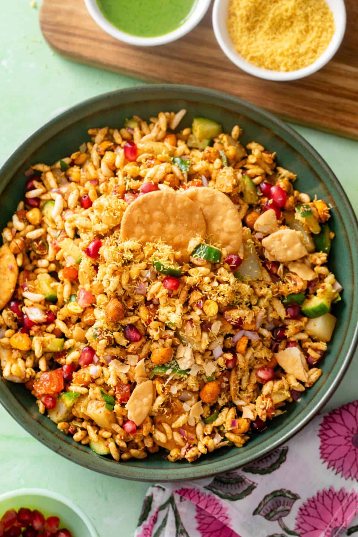 To view image of Bhel puri chaat served in a green bowl with extra sev and chutney.