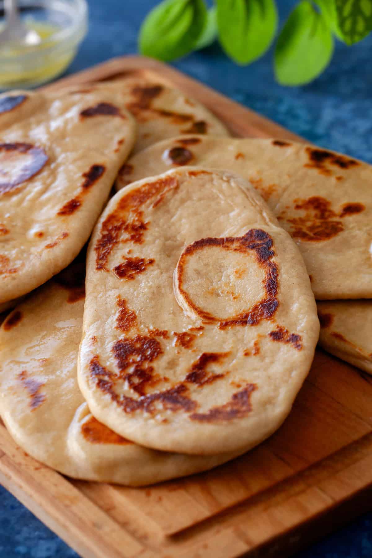 A side image of lot of atta naan placed on a wooden board with bowl of melted butter in background.