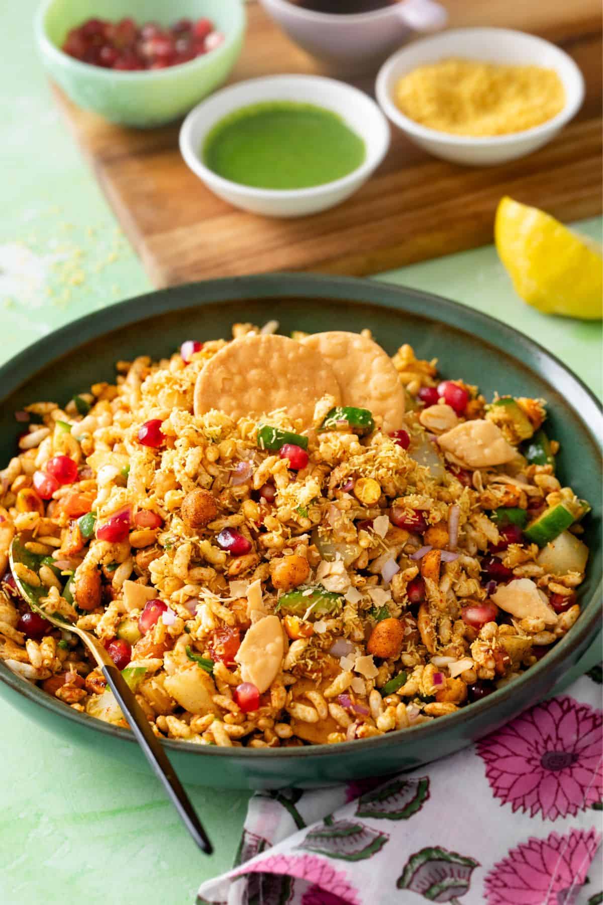 Bhel puri chaat served in a shallow green bowl with sev, pomegrante and chutney.