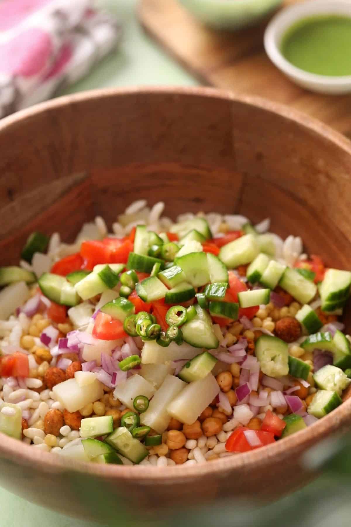 Bhel ingredients and chopped vegetables in a large wooden bowl.