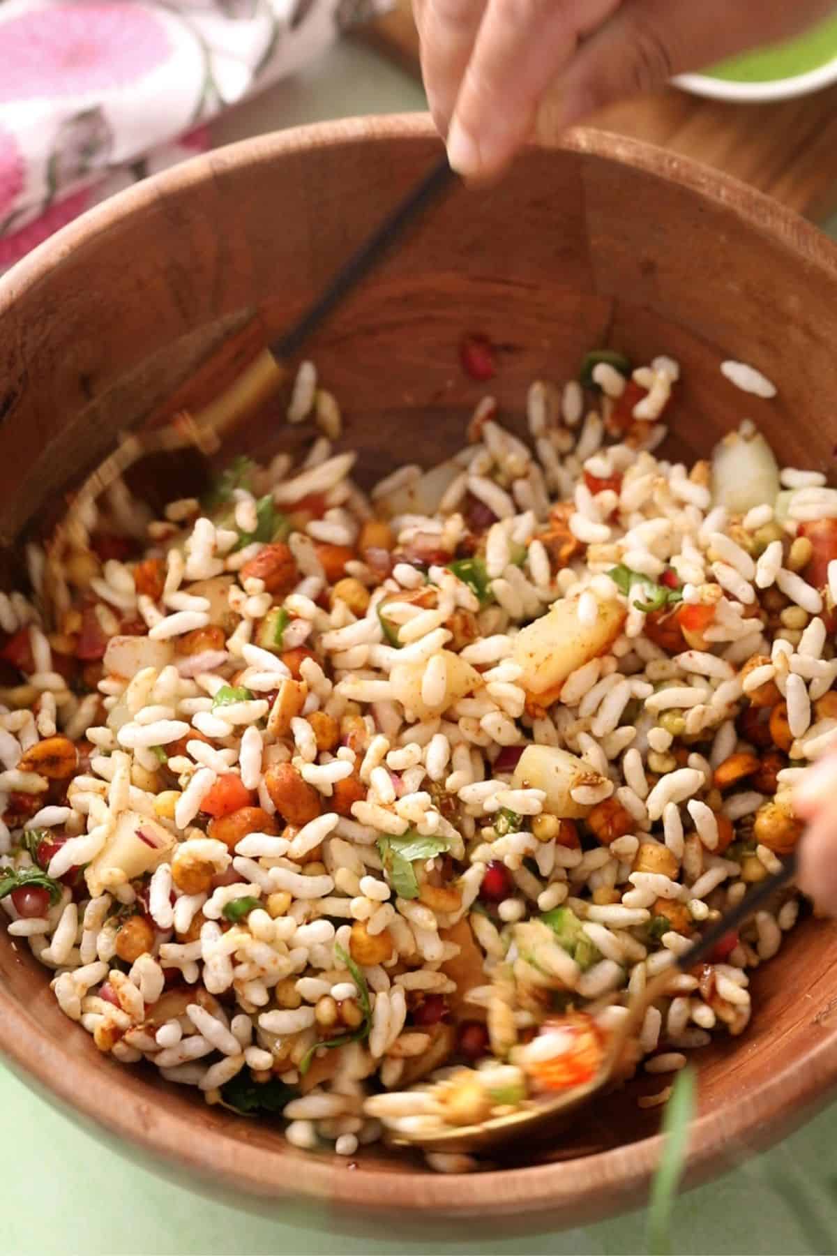 Bhel is being tossed together using two gold and black spoons.