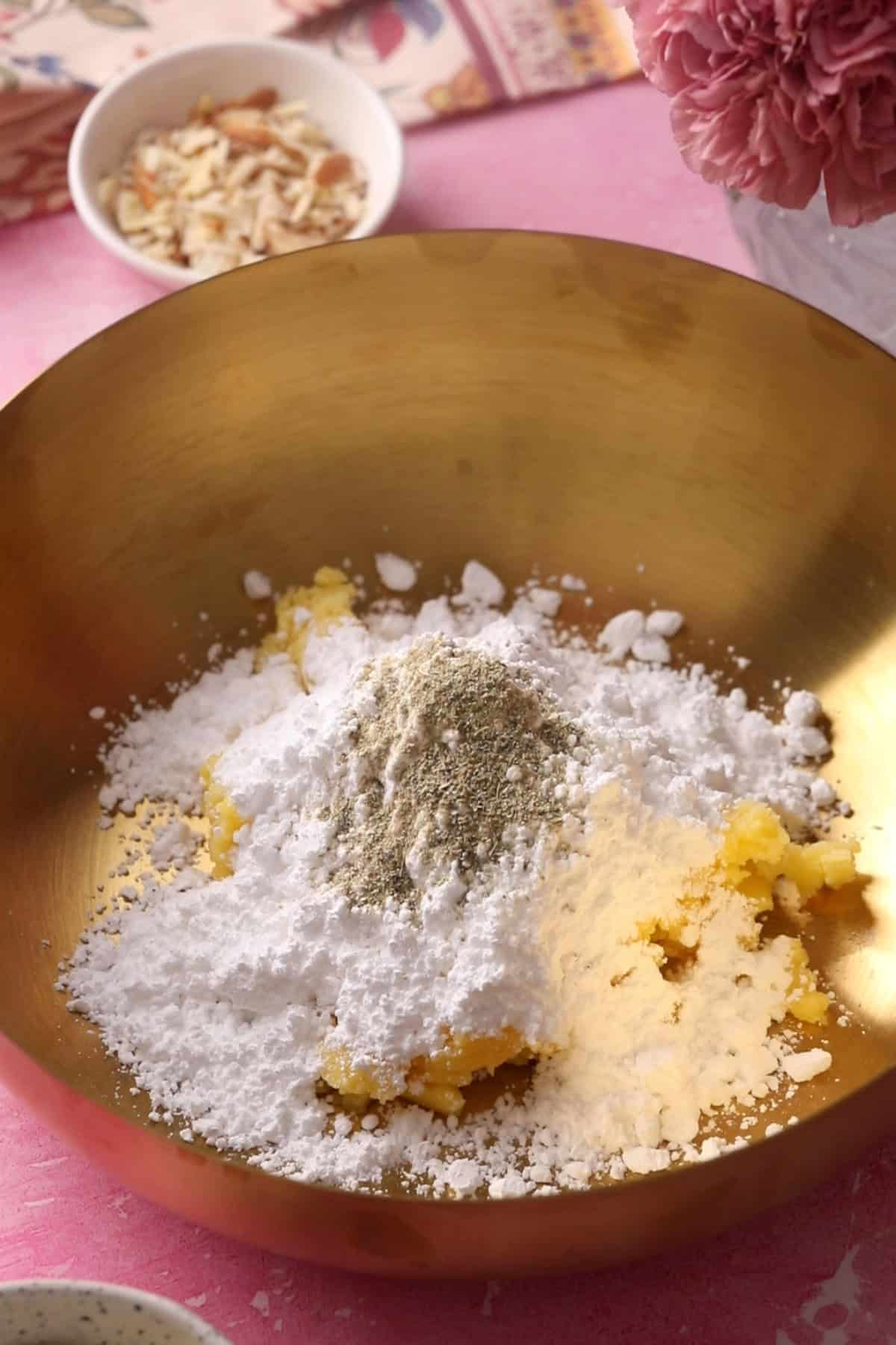 Ghee, sugar and cardamom powder are placed in a gold mixing bowl.