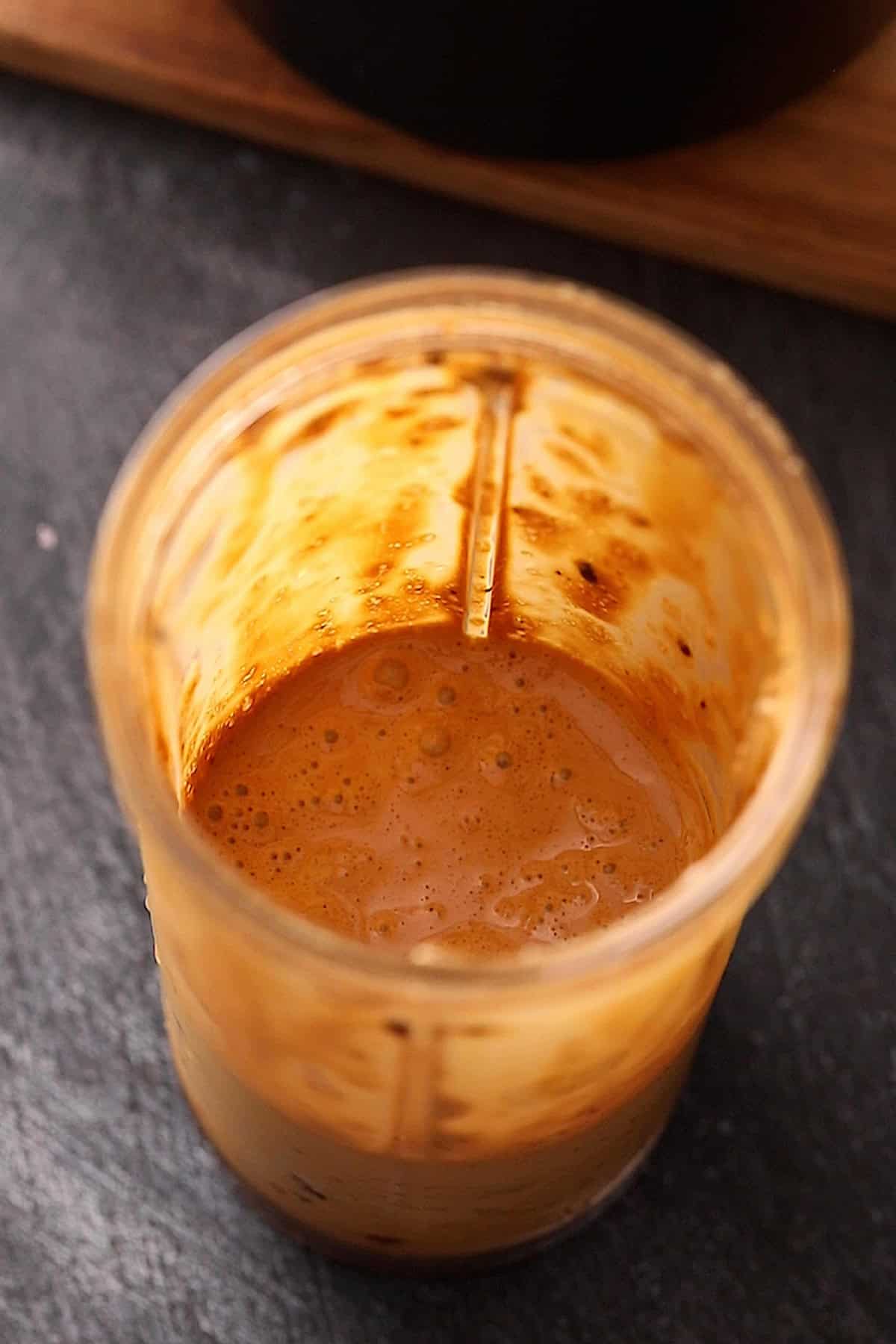A blender cup with frothy coffee slush with splatters on the sides.