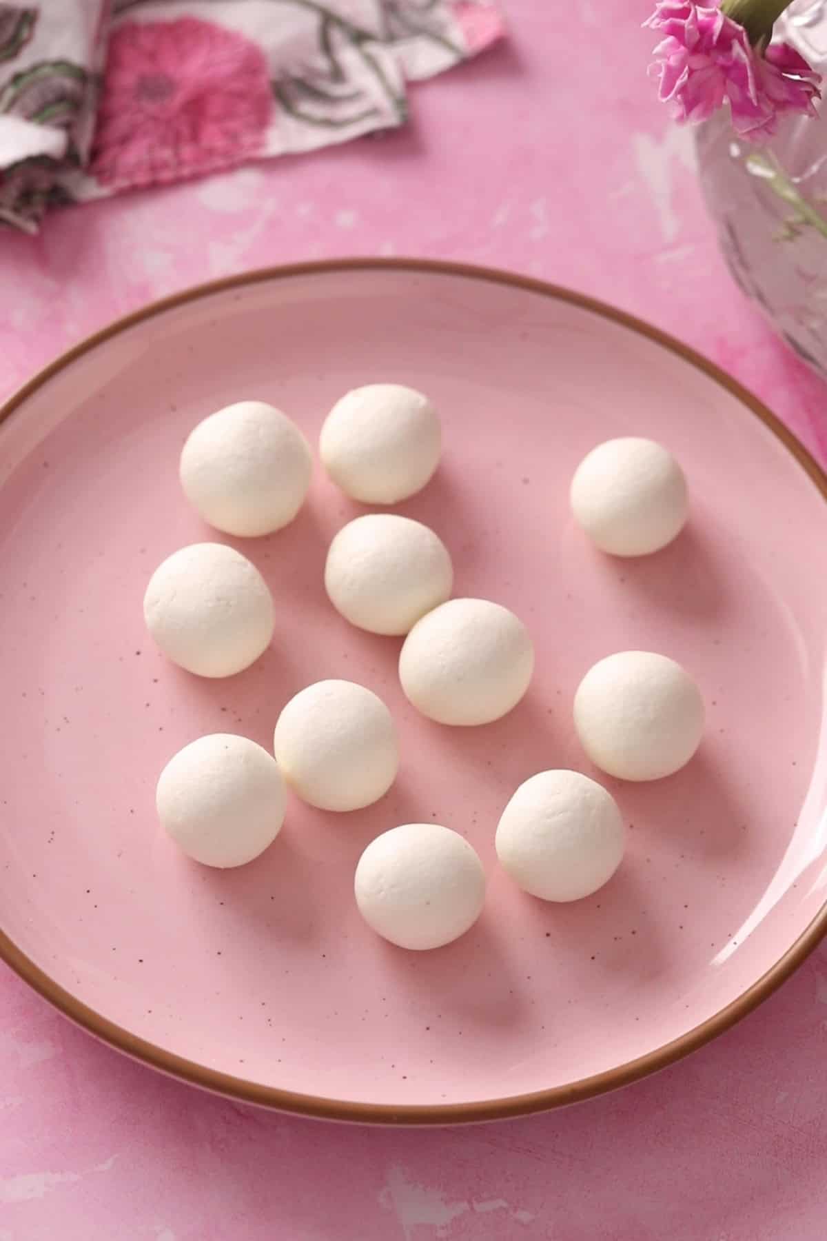 Rolled uncooked rasgulla are placed on a pink plate.